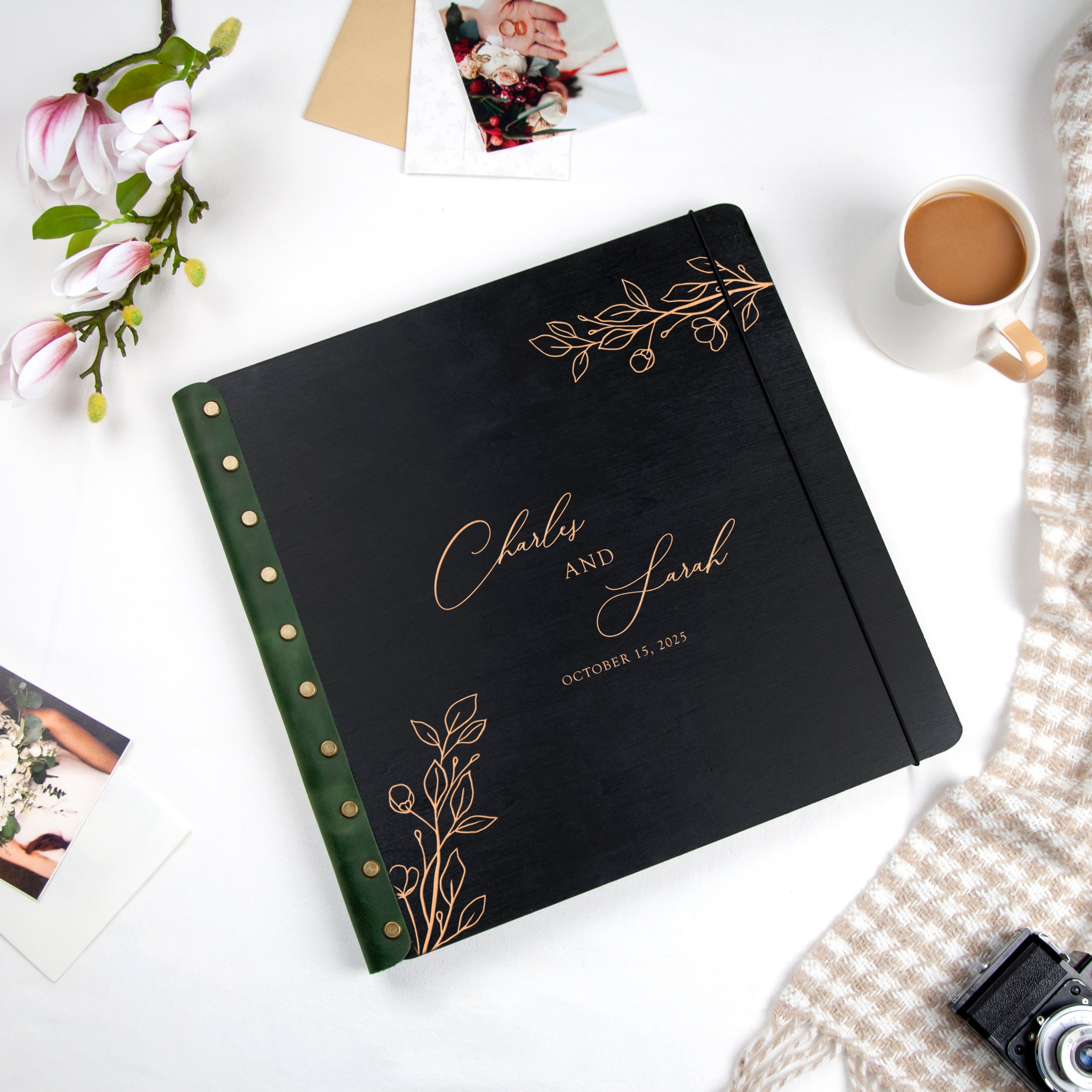 a black photo album with gold leaf designs, a cup of coffee, and some photographs and stationery items on a white surface.