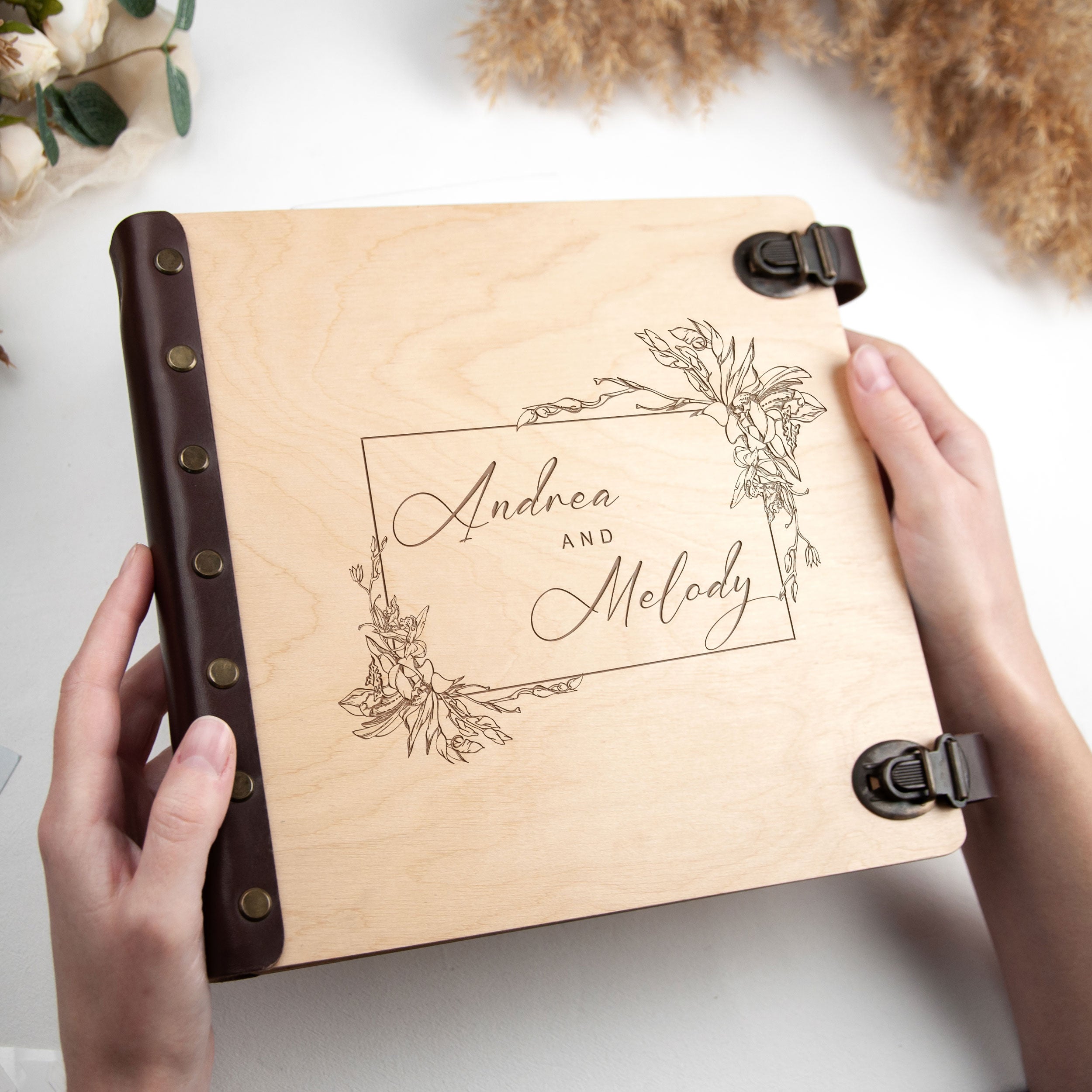 A person is holding a wooden photo album with the names 'Andrea and Melody' engraved on it.