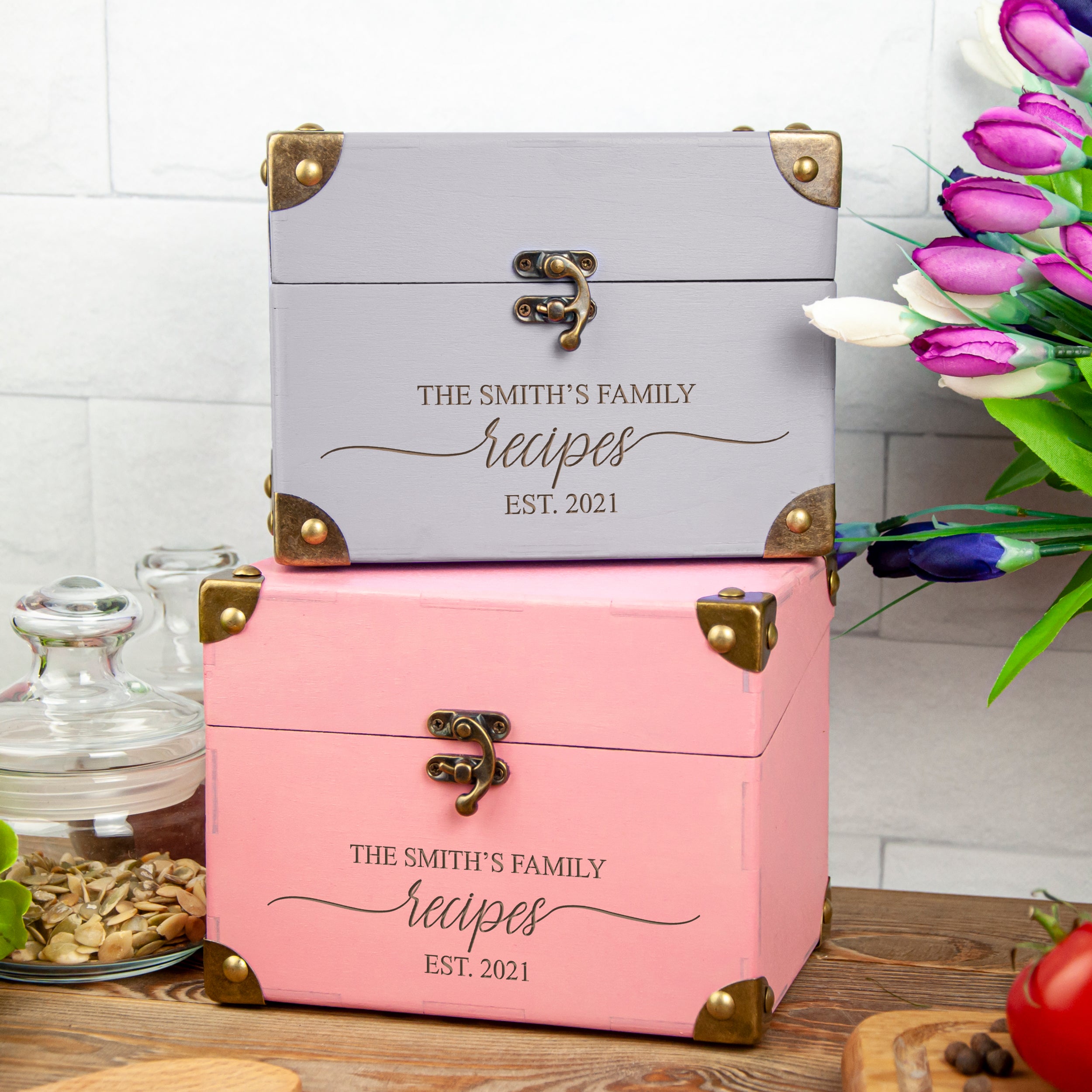 Two wooden recipe boxes with brass clasps and the text "The Smith's Family Recipes EST. 2021" printed on them, placed on a wooden surface.