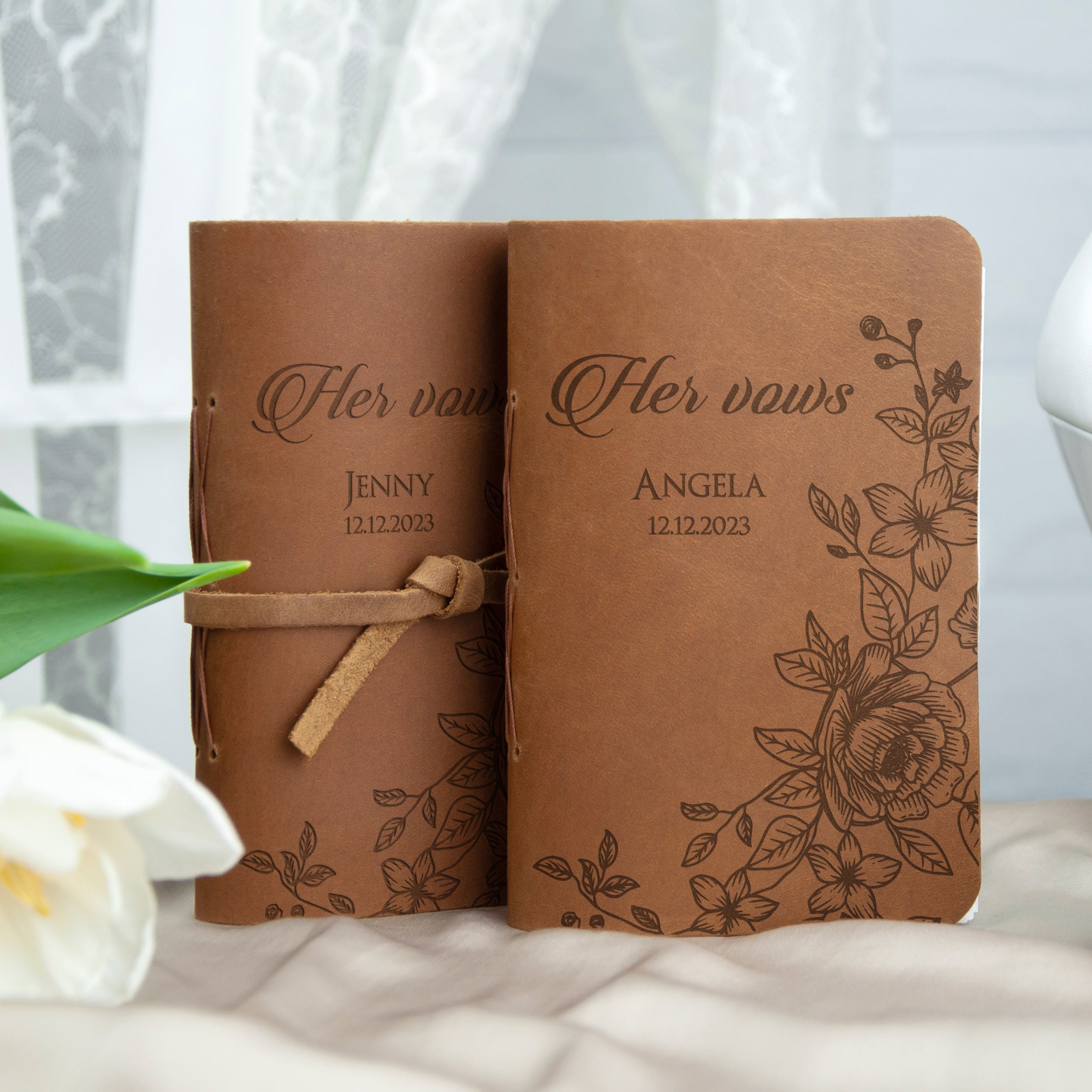 Two brown leather-bound notebooks with floral designs and text, likely wedding vows, are placed on a white surface.
