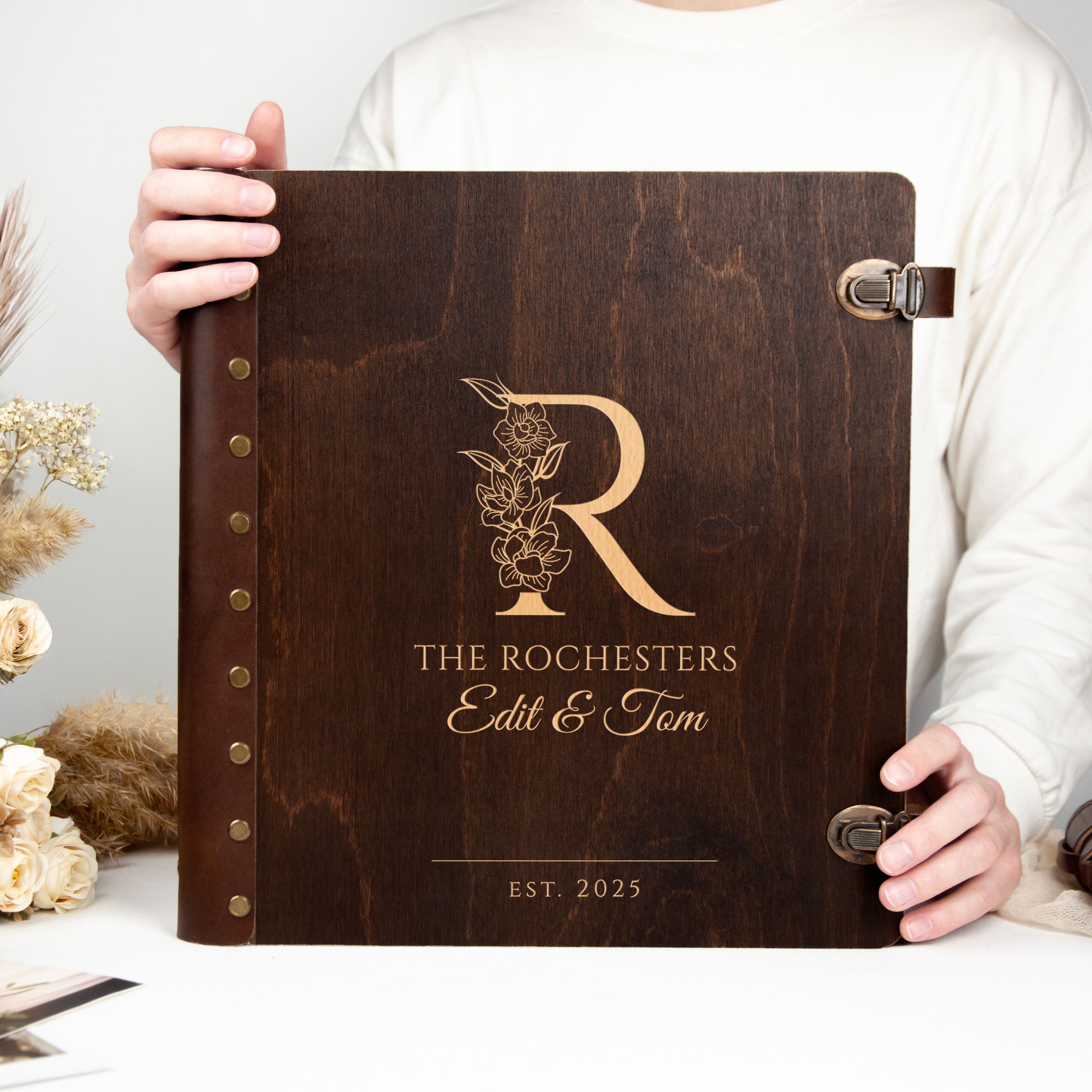 A person is holding a wooden album or binder with a gold letter "R" and text printed on it.