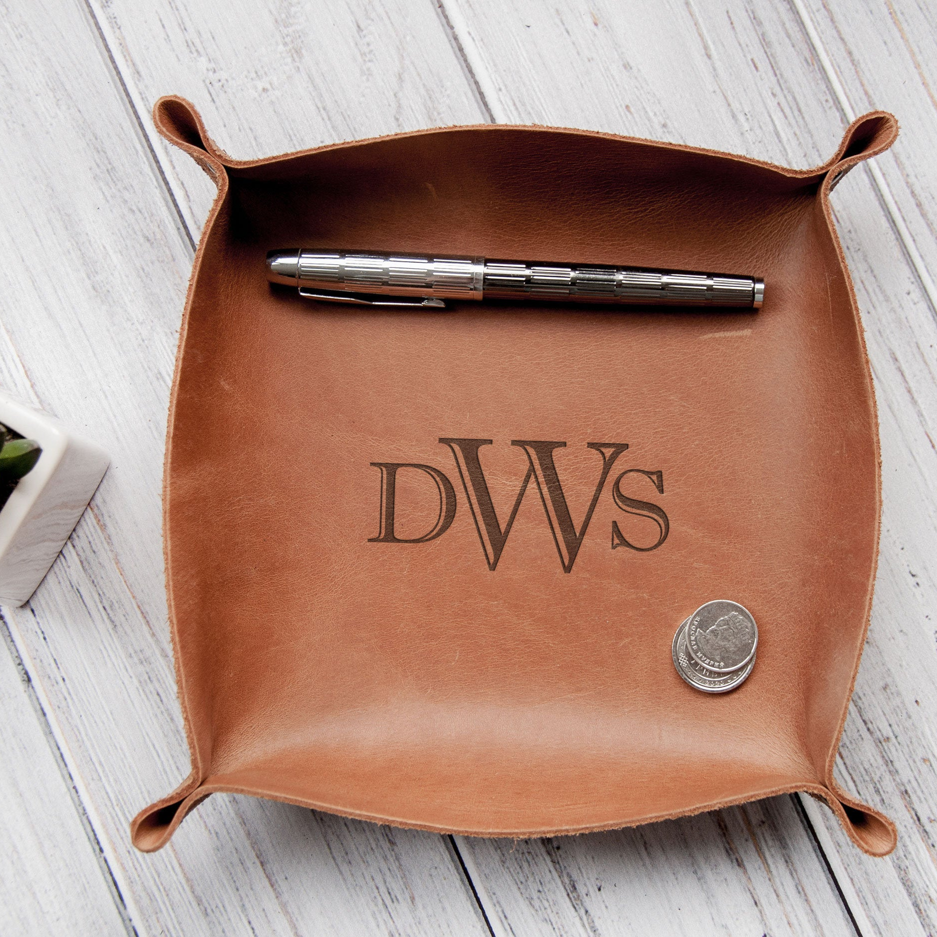 A brown leather desk organizer with a pen and a coin inside, placed on a wooden surface.