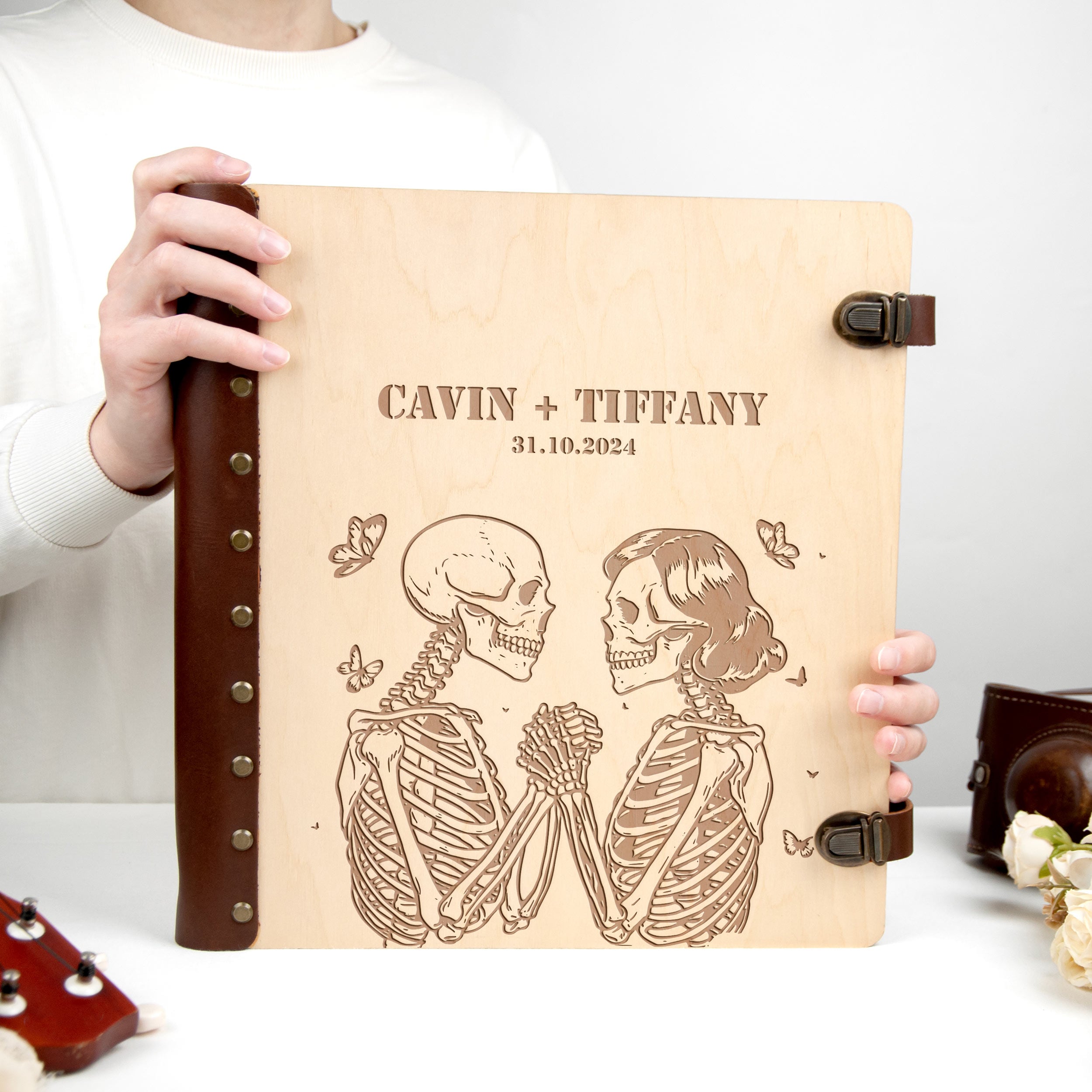 A person is holding a wooden album with a skeleton design and text on it.