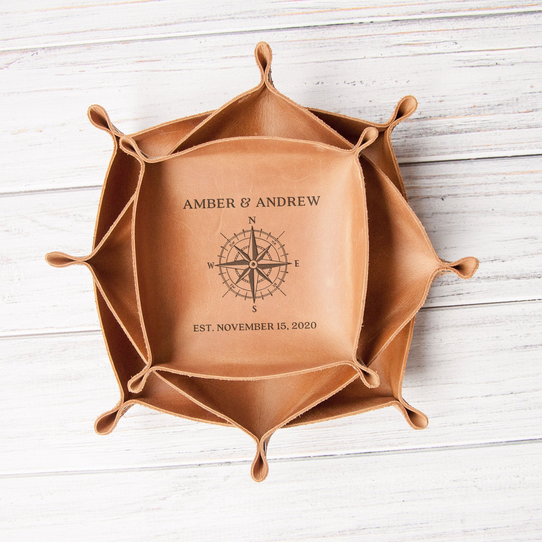 A leather tray with a compass design and the names 'Amber & Andrew' printed on it, placed on a white wooden surface.