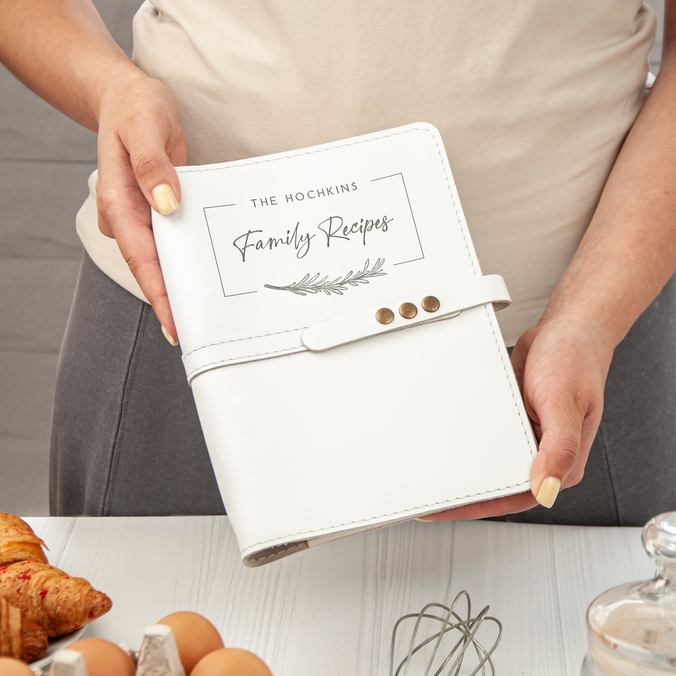 A person is holding a white recipe book with the title "The Hochkins Family Recipes" printed on it.