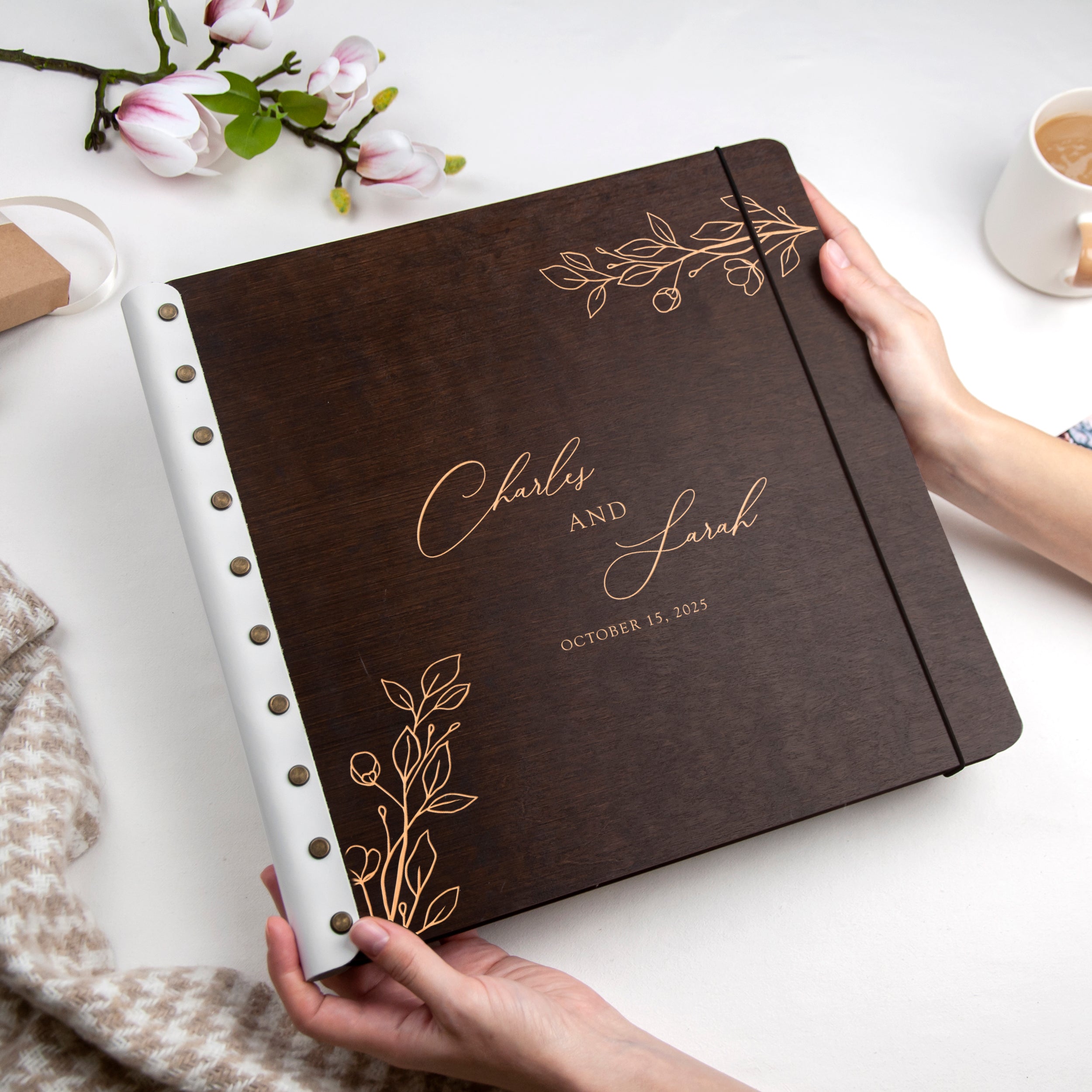 A person is holding a brown leather-bound book with gold leaf designs, which appears to be a wedding album or scrapbook.