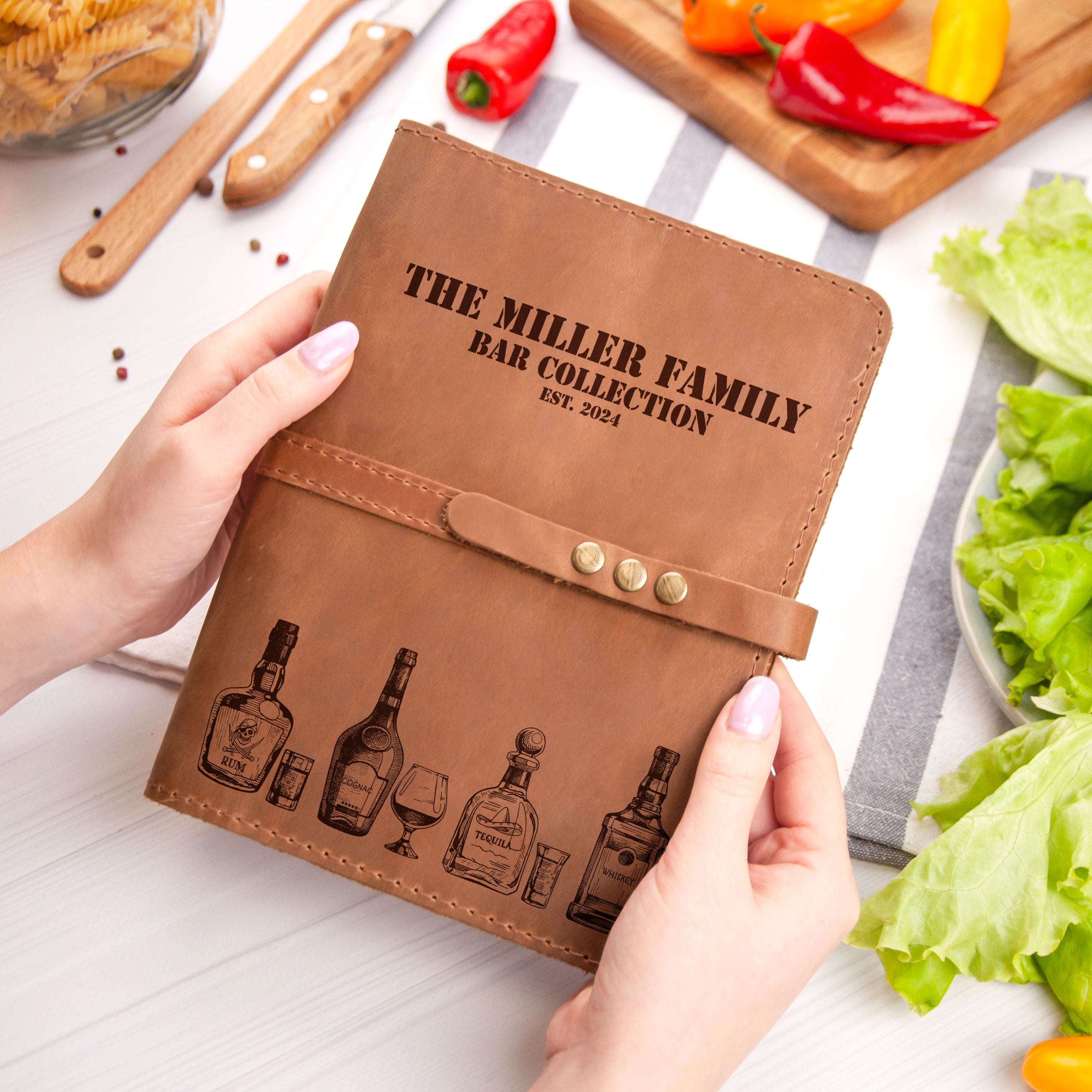 A person's hands holding a leather-bound book titled "The Miller Family Bar Collection" with illustrations of various alcoholic beverages on the cover.