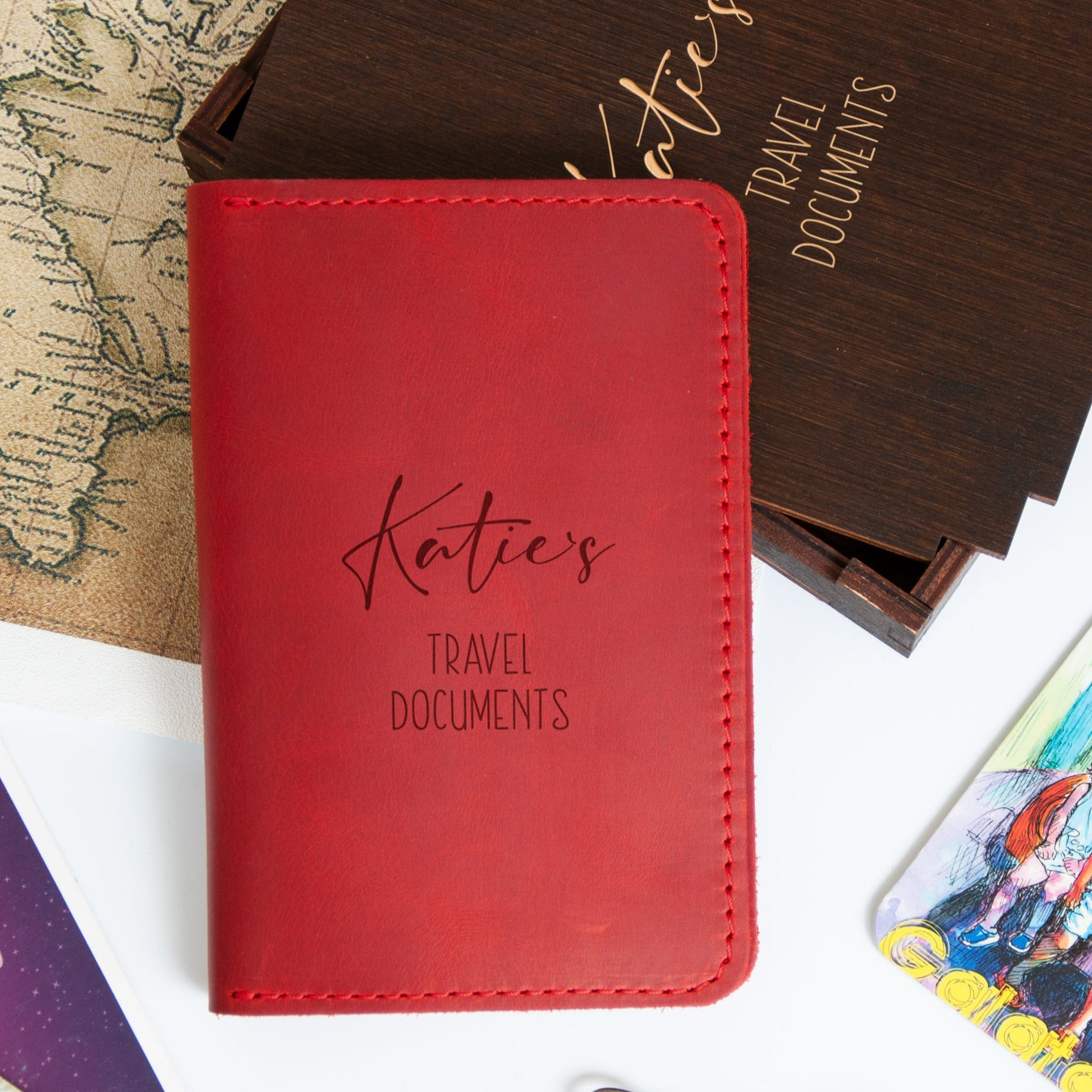 A red travel document holder with the name "Katies" printed on it, placed on top of a wooden box with the word "Travel Documents" written on it.