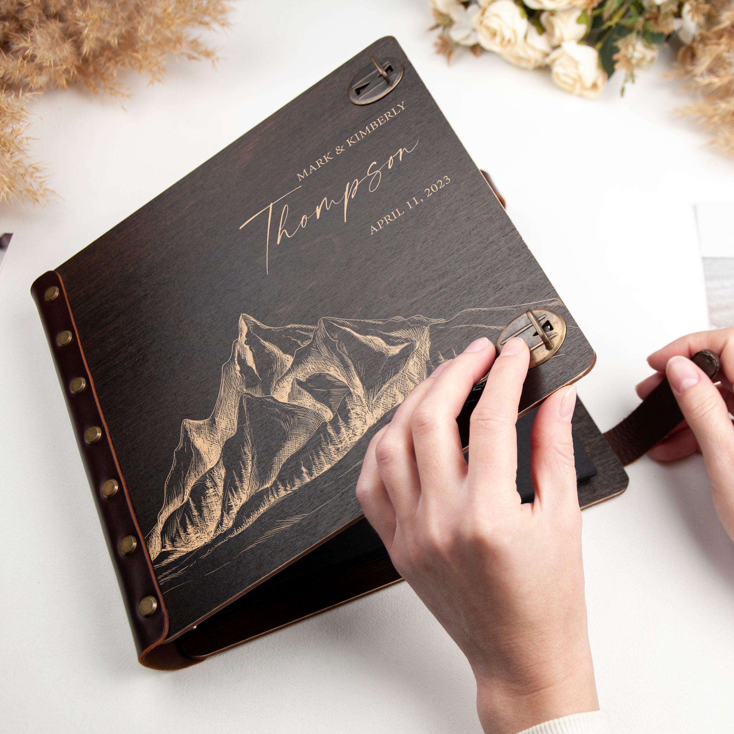 A person's hands are holding a black leather-bound book with a mountain illustration on the cover.