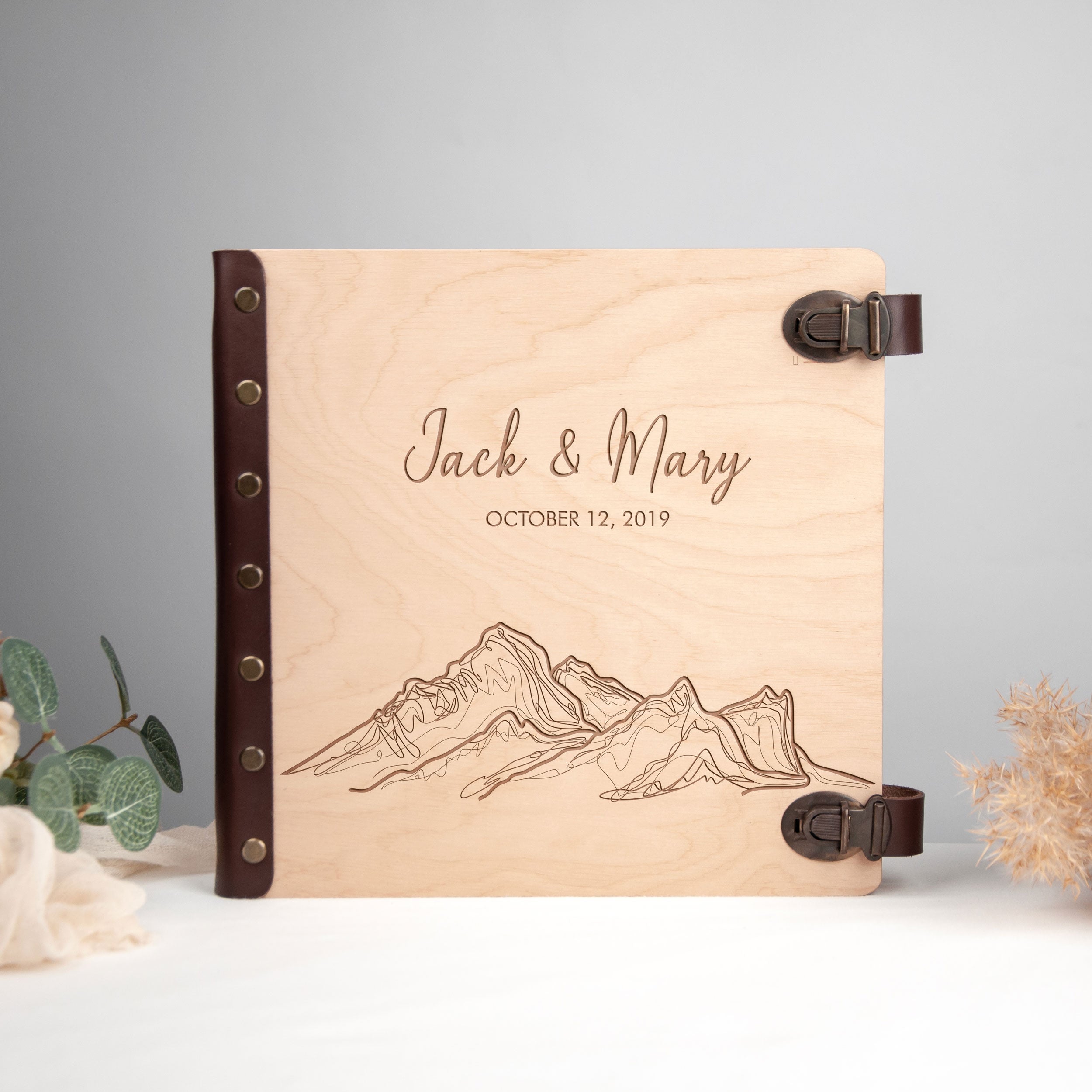 A wooden photo album with a mountain landscape engraved on it, featuring the names 'Jack & Mary' and the date 'October 12, 2019'.