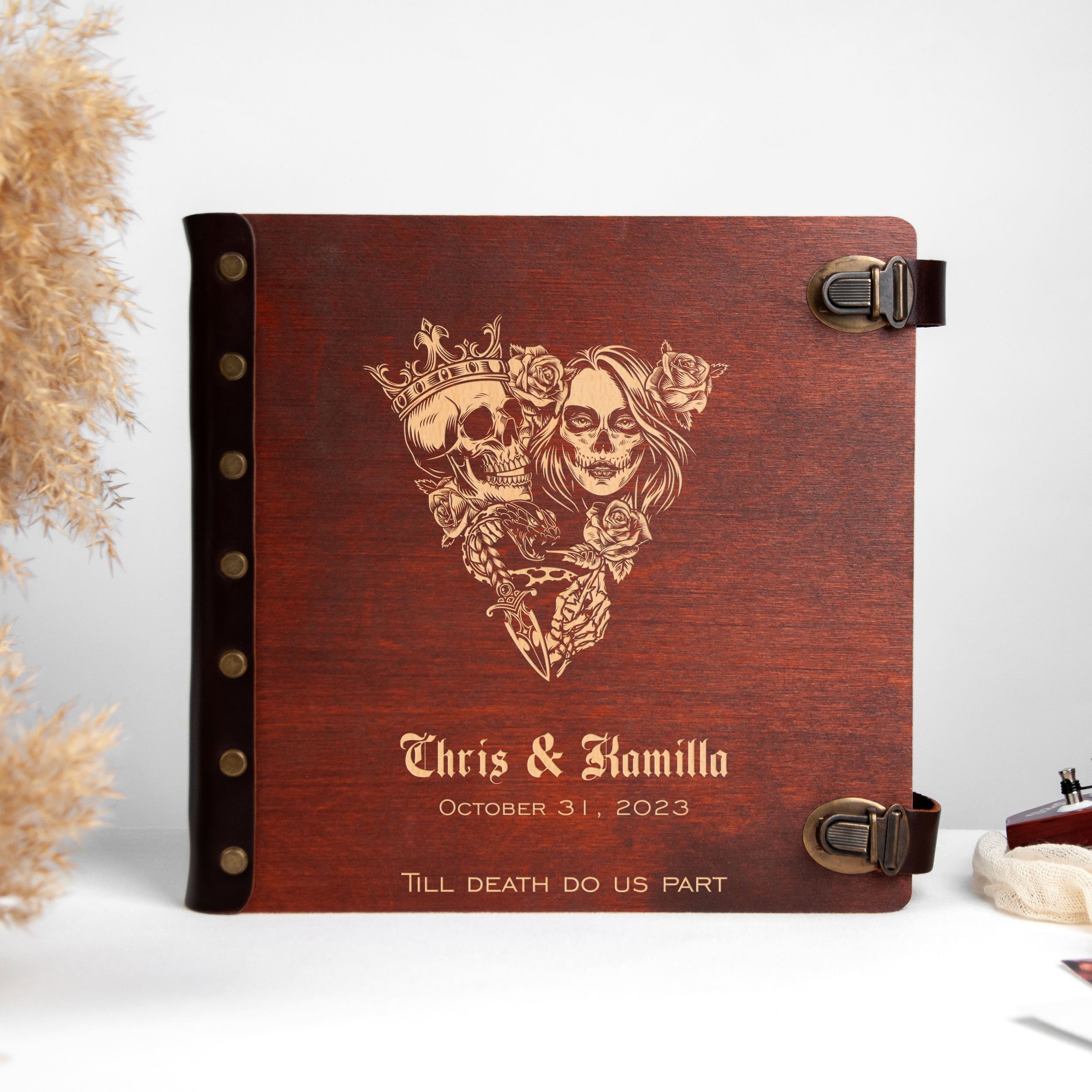 A wooden album with a decorative design featuring a skull and rose motif, and the names 'Chris & Kamilla' printed on it.