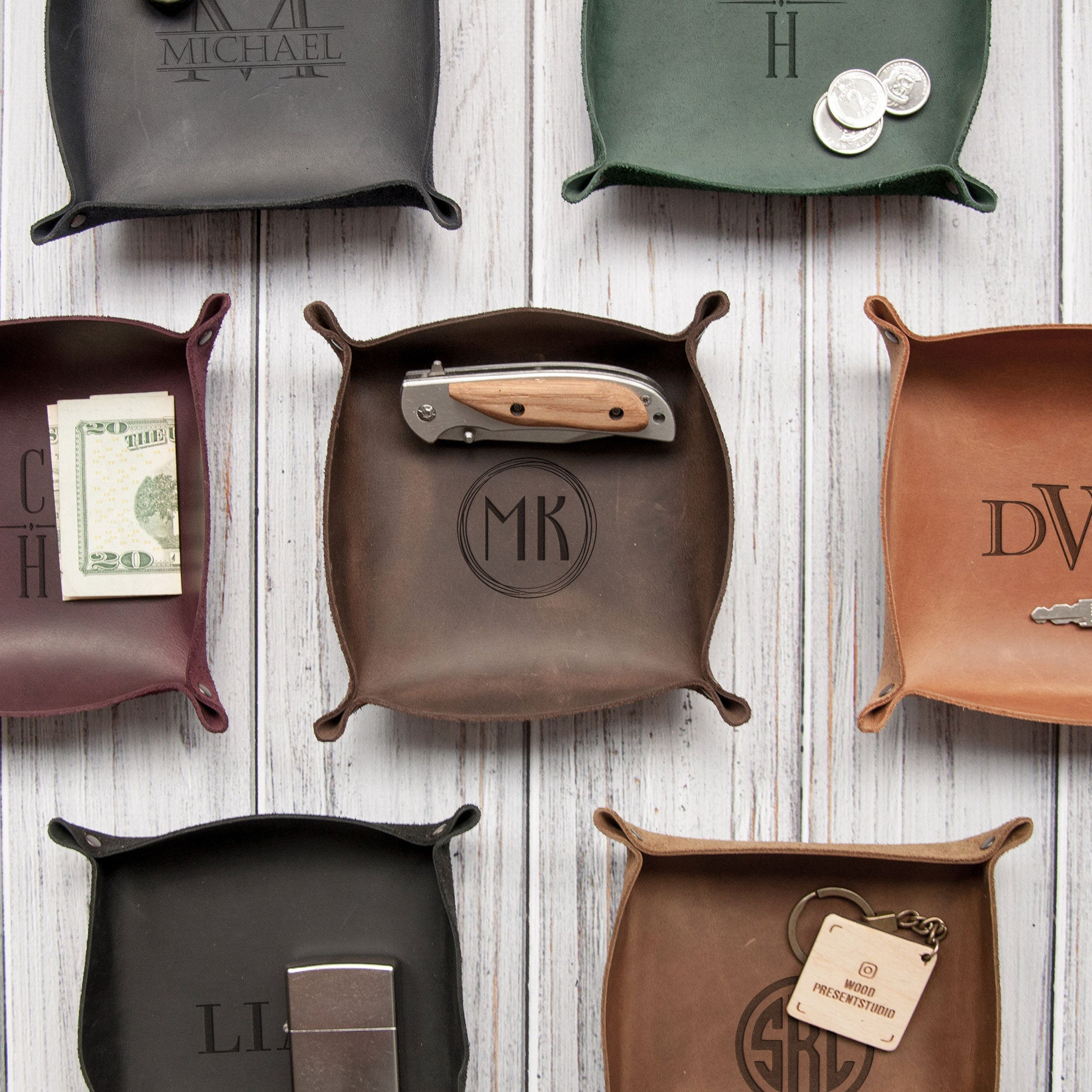 a collection of leather trays and containers, each with a personalized monogram or initials engraved on them. The trays are arranged on a wooden surface, creating an organized and visually appealing display.