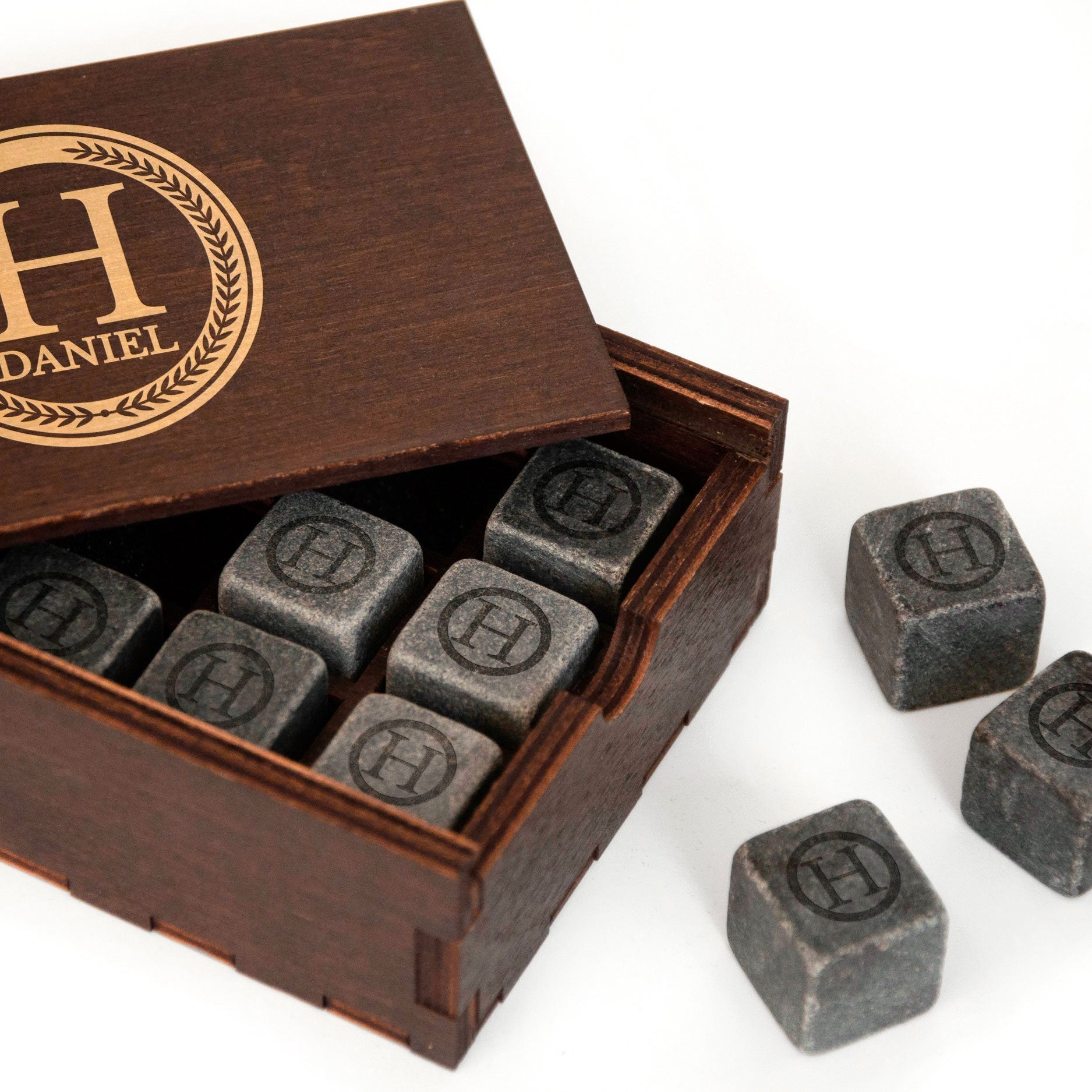 A wooden box containing several gray stone cubes with a gold "H" logo on them, along with some additional gray stone cubes.