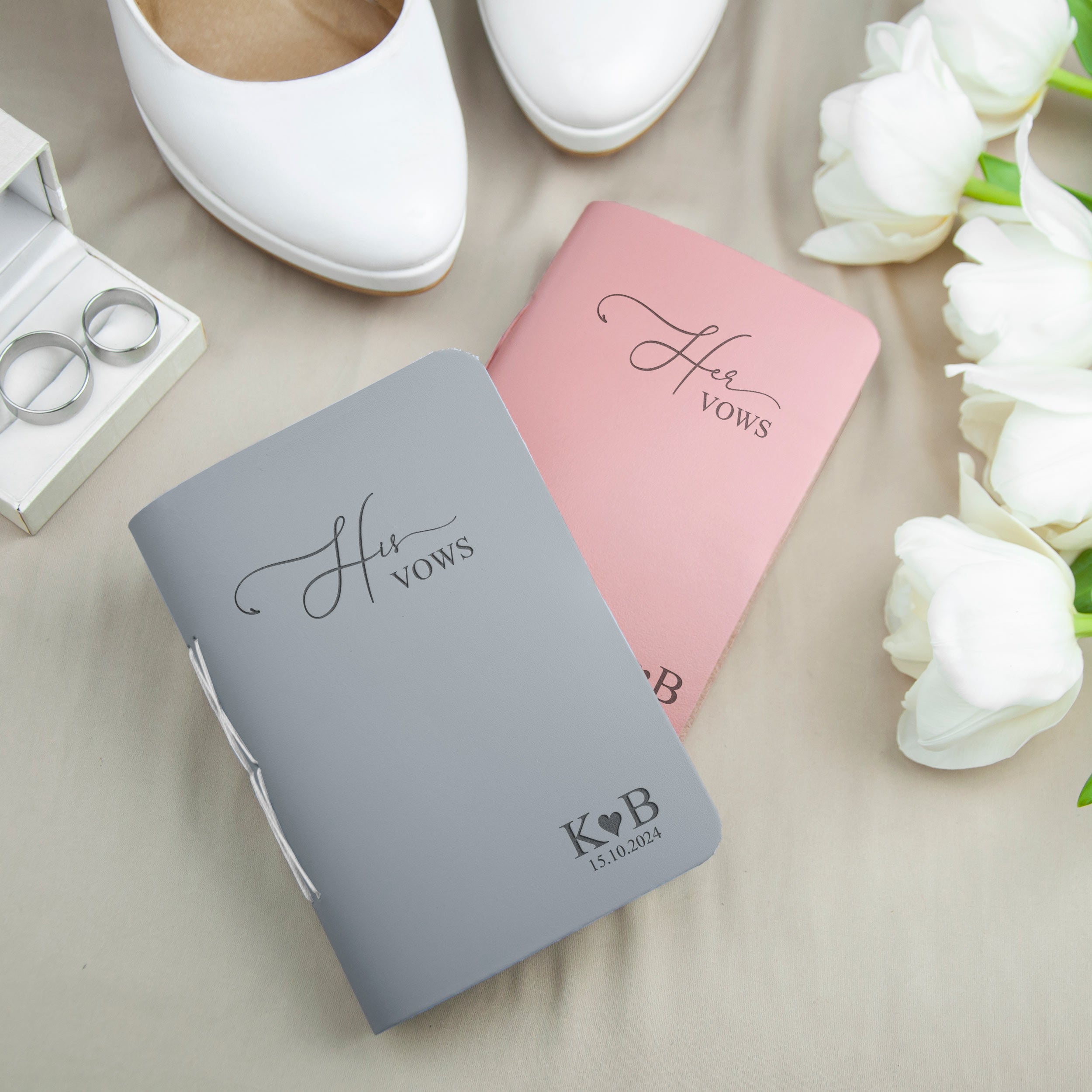 a pair of gray and pink wedding vows books, a pair of white shoes, and a bouquet of white roses, all arranged on a beige background.