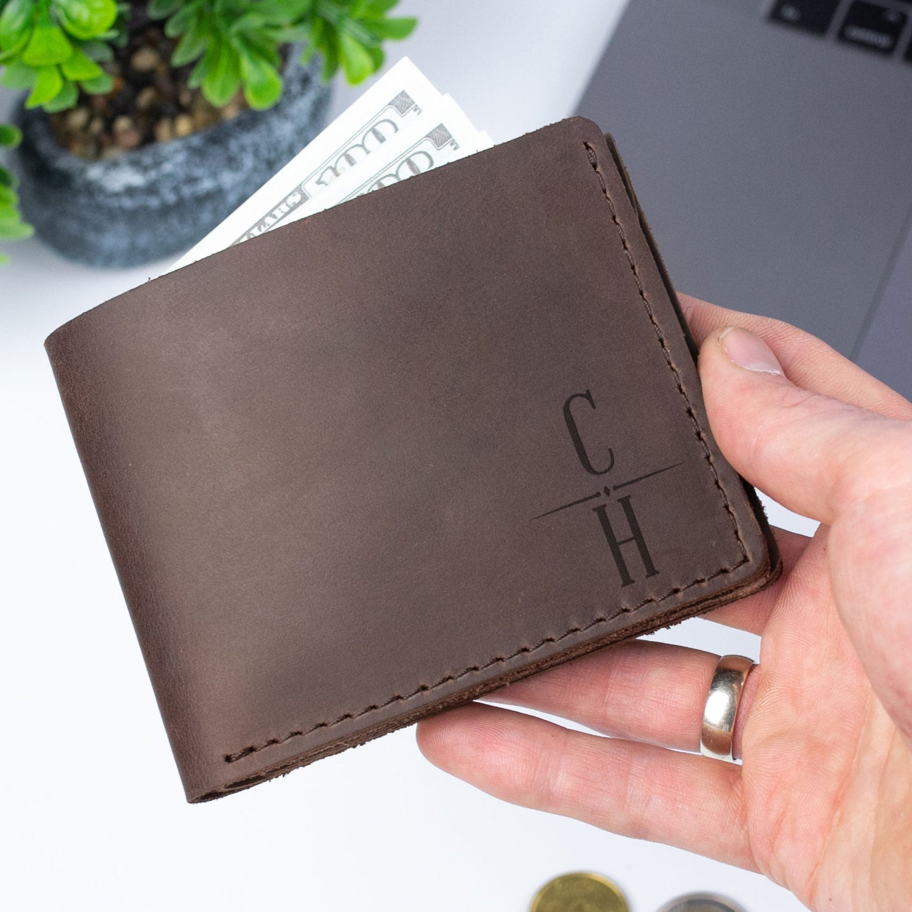 A hand holding a brown leather wallet with a monogrammed initials on it.