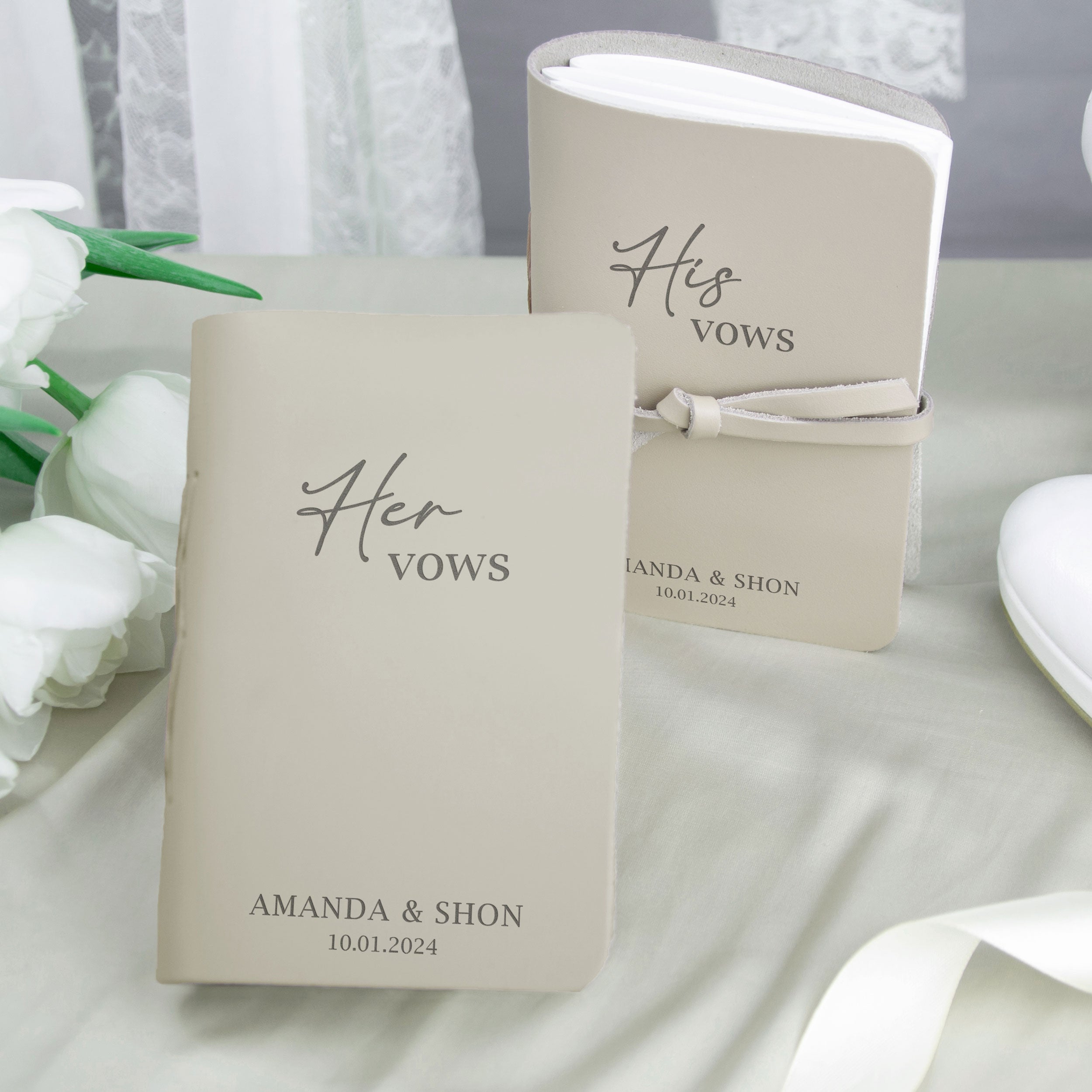 two beige-colored notebooks with the text "Her Vows" printed on them, placed on a table with white flowers.