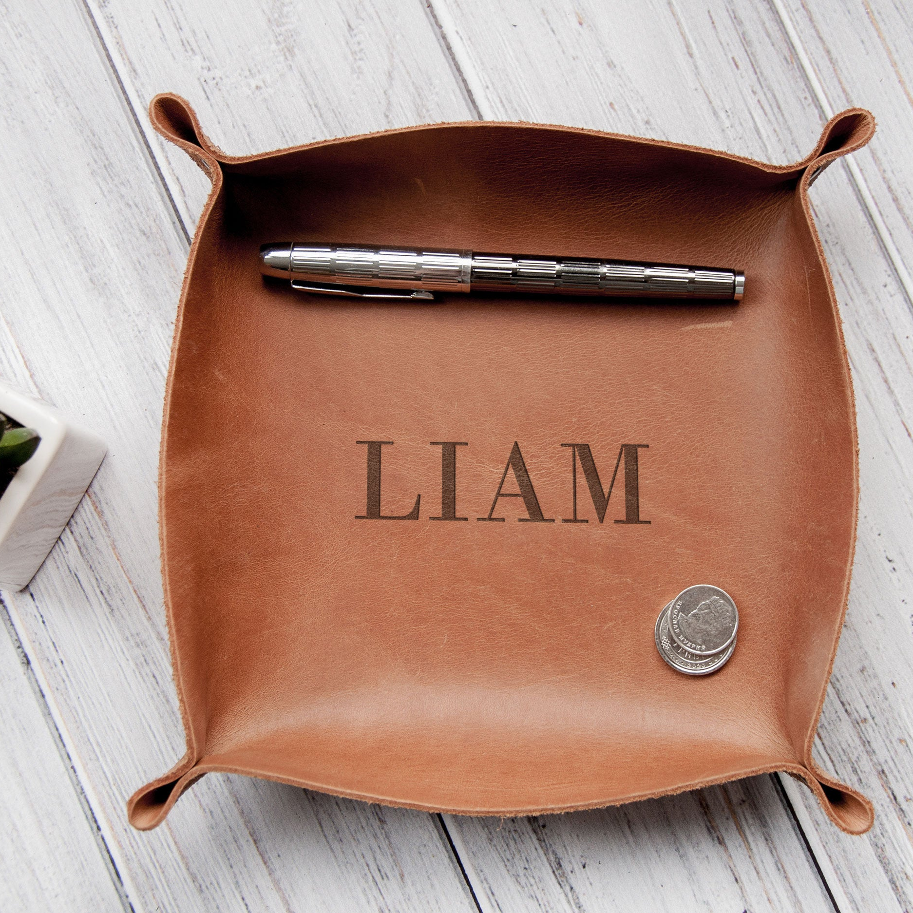 A leather desk organizer with a pen and a coin inside, placed on a wooden surface.