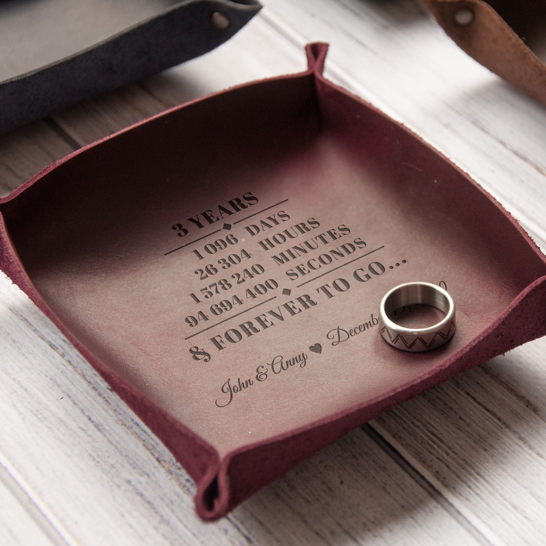 A personalized leather tray with a 3-year anniversary message engraved on it, along with a wedding ring placed on top of the tray.