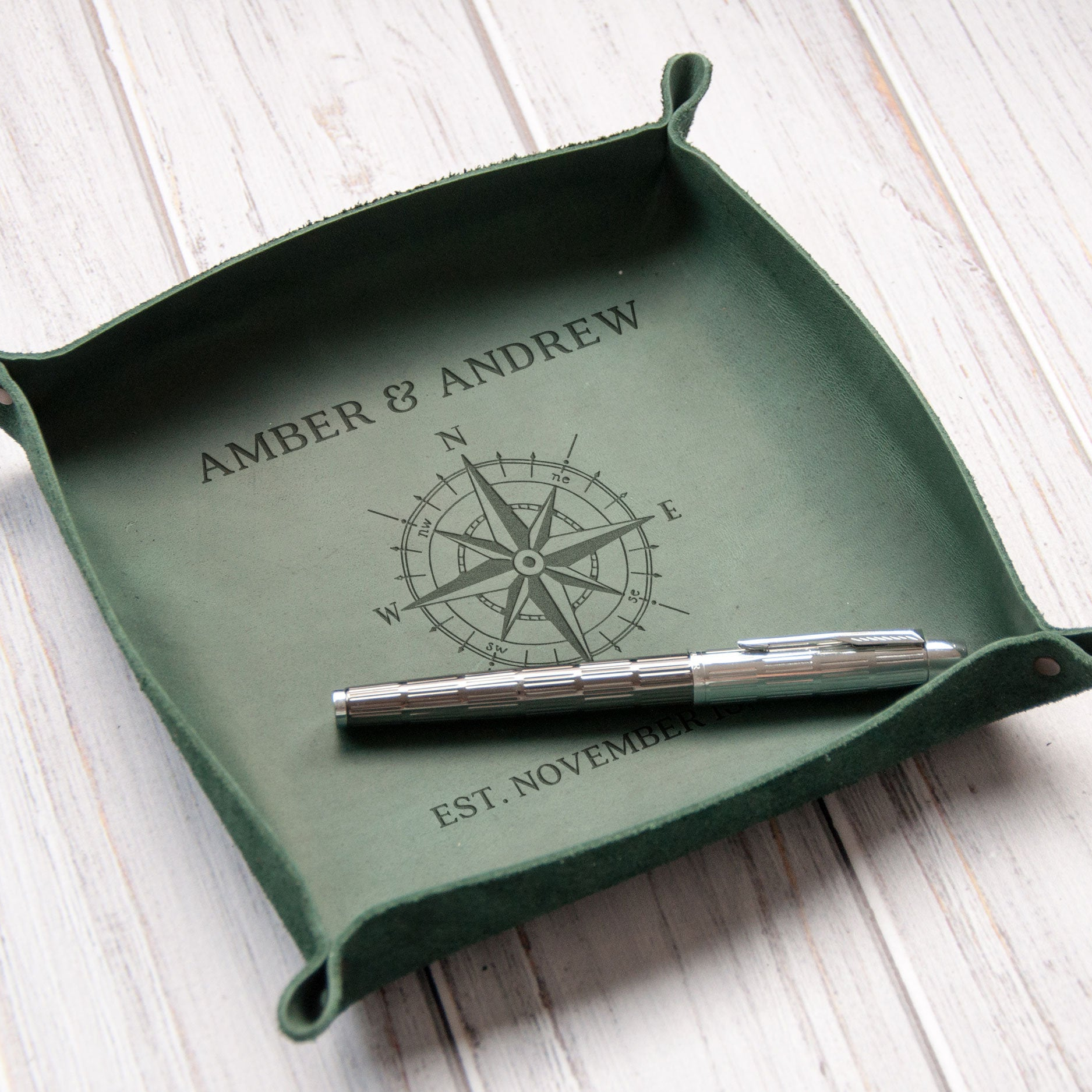 A green leather tray with a compass design and the names "Amber & Andrew" printed on it, along with the text "EST. NOVEMBER" below the compass.