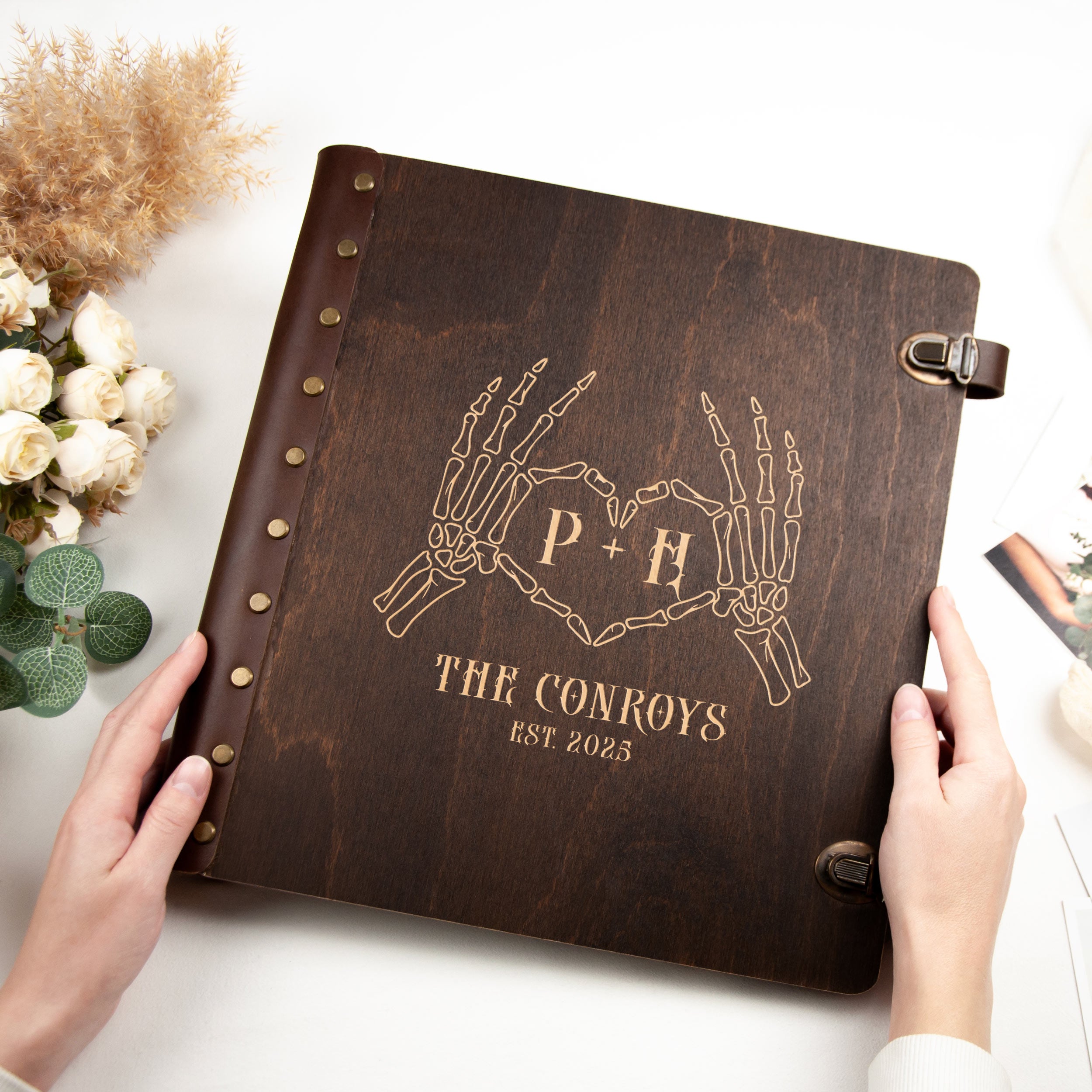 A person's hands holding a wooden photo album with a skeleton handprint design and text on the cover.
