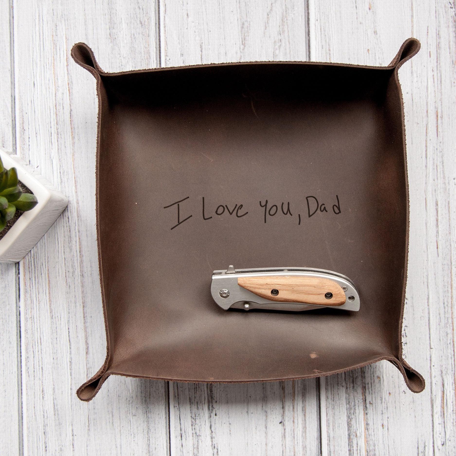 A brown leather tray with a handwritten message that reads "I Love You, Dad" placed on top of a silver pocket knife.
