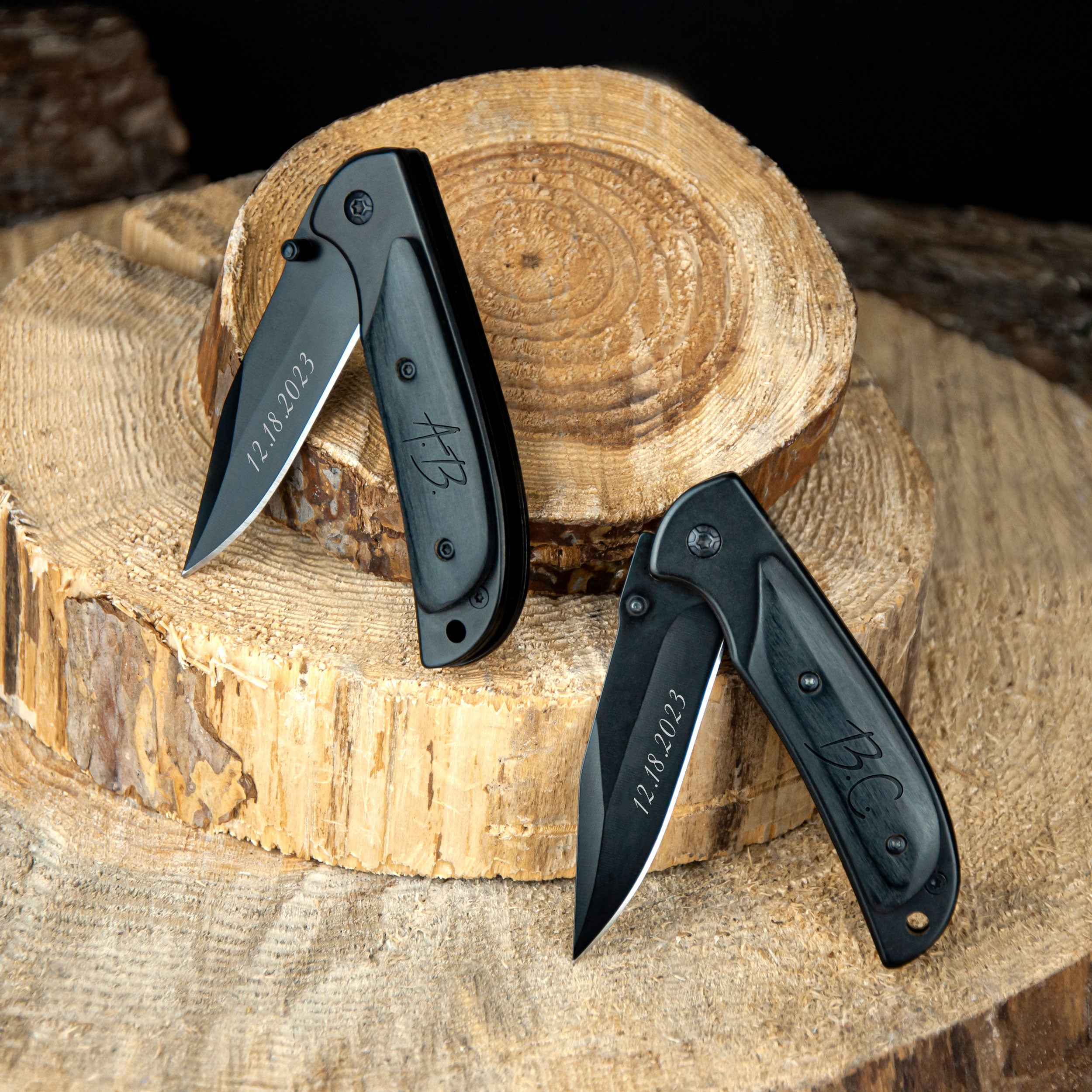 three black pocket knives with engraved dates on them, placed on a wooden surface.