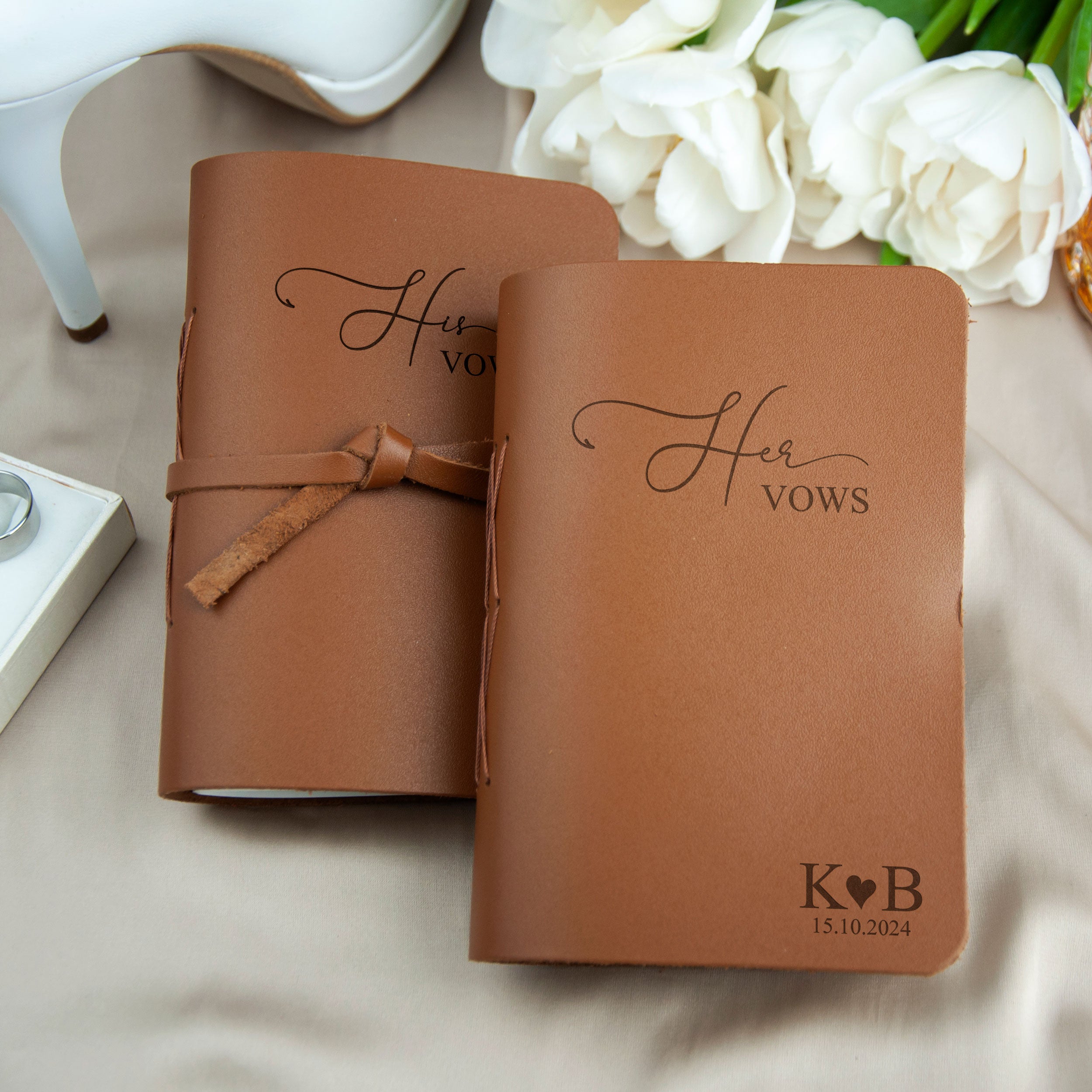 Two leather-bound notebooks with the text "Her Vows" printed on them, along with a pair of white roses and a pair of white shoes.