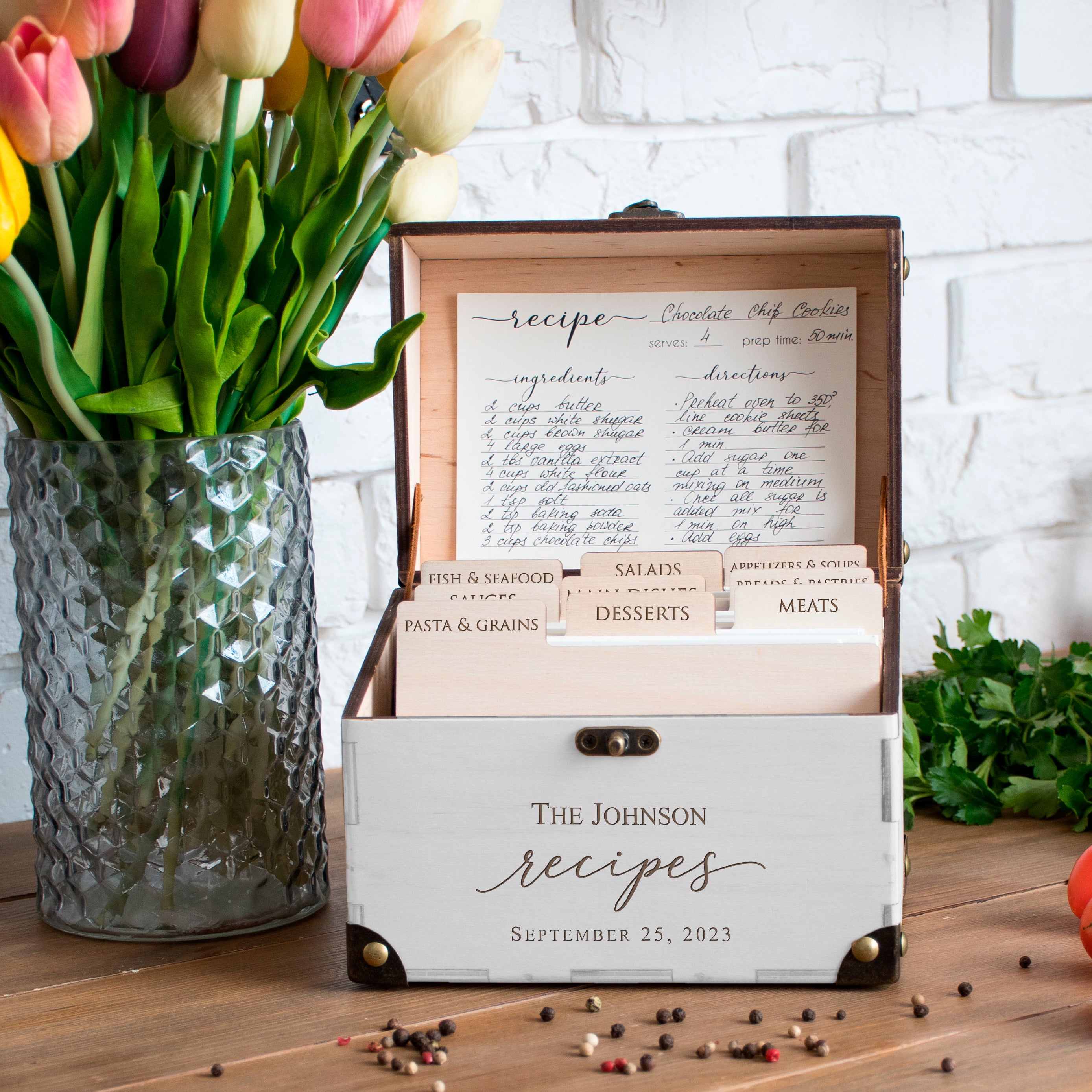 a wooden recipe box with a vase of tulips and a bowl of fresh herbs on a wooden table.