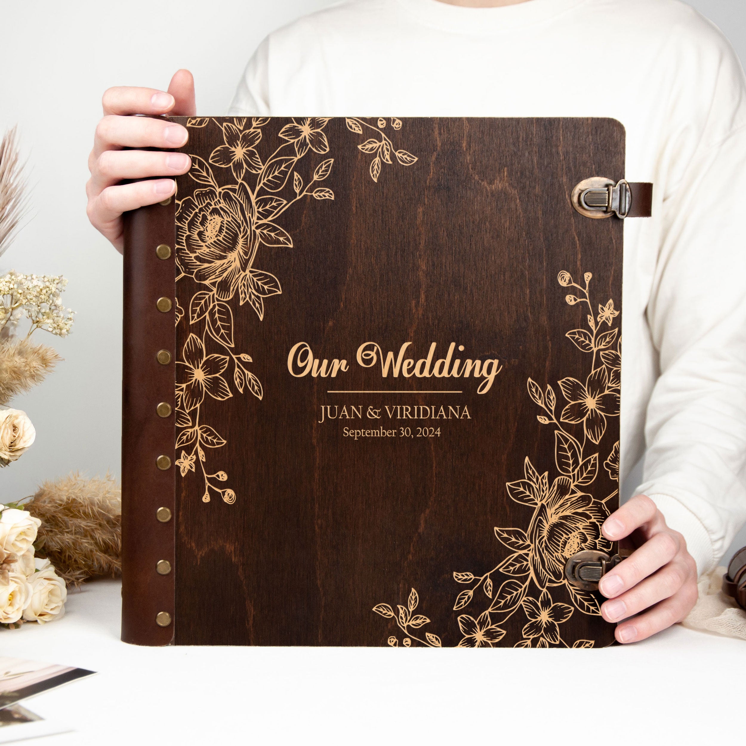 A person is holding a wooden wedding album with gold floral designs and text.