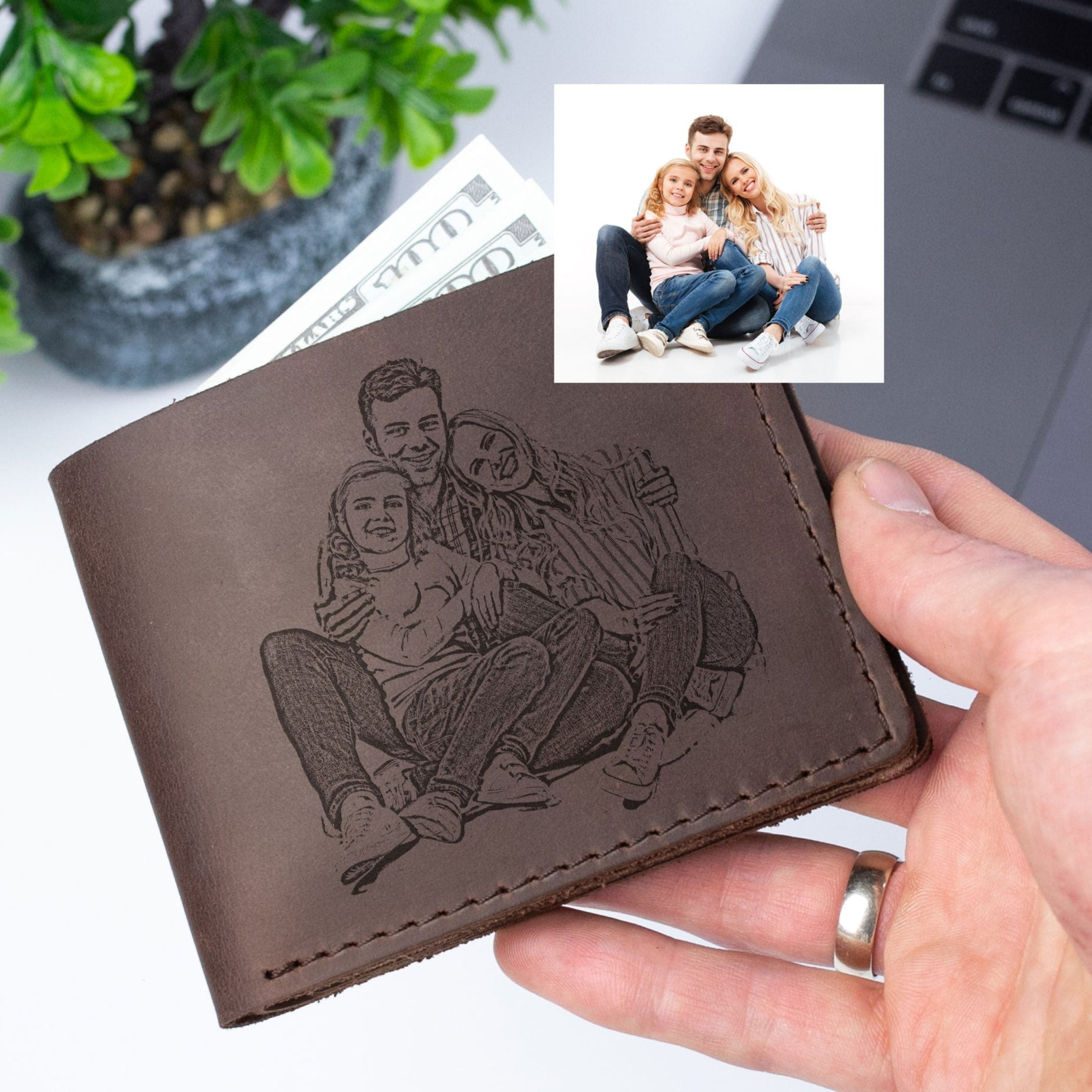 A hand holding a wallet with a personalized engraved image of a family, including a man, woman, and child.