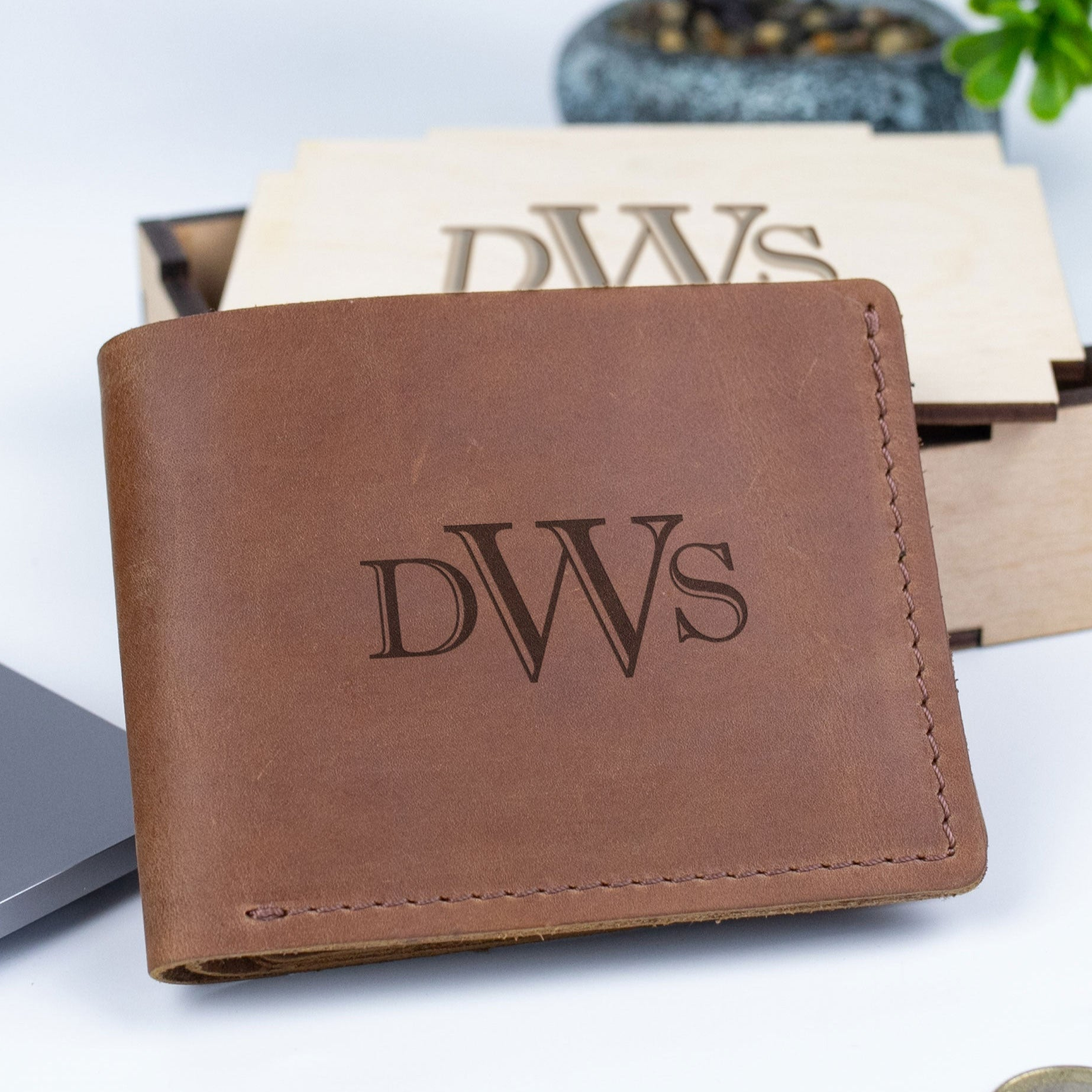 A brown leather wallet with the initials "DWS" engraved on it, placed on a white surface.
