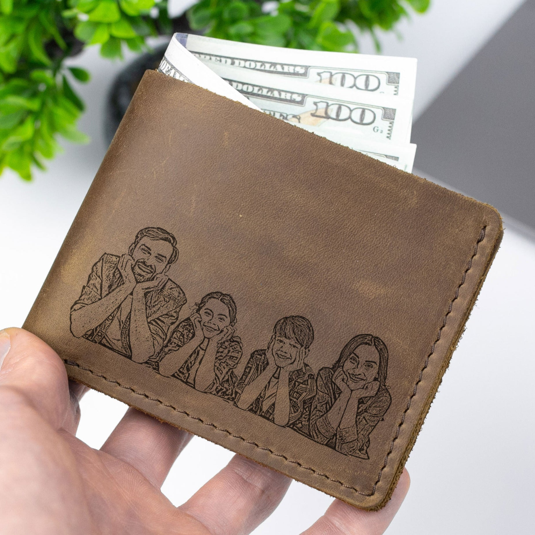 A hand holding a wallet with a personalized engraved image of four smiling people on it.