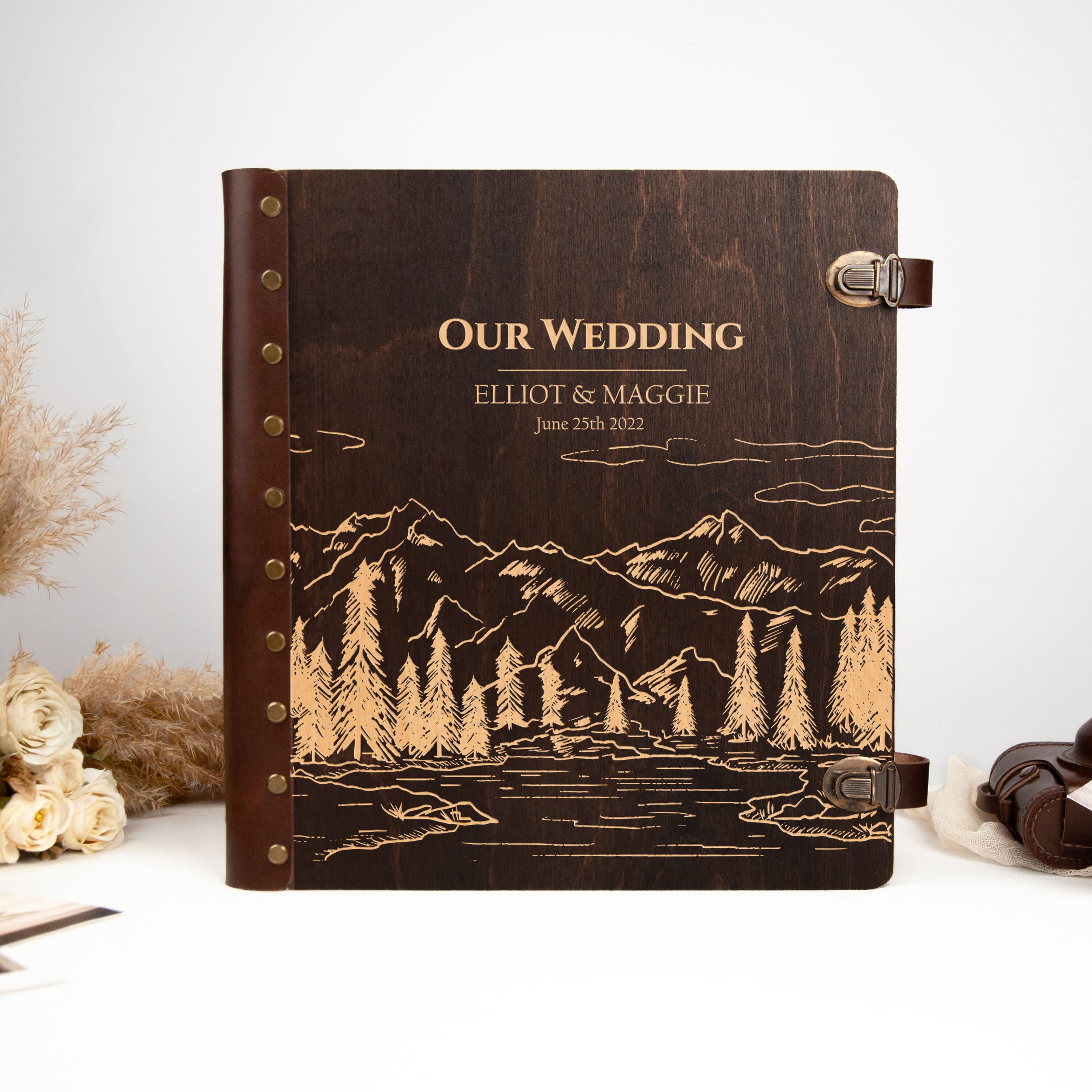 A wooden wedding album with a mountain landscape engraved on the cover, featuring the names 'Elliot & Maggie' and the date 'June 29, 2012'.