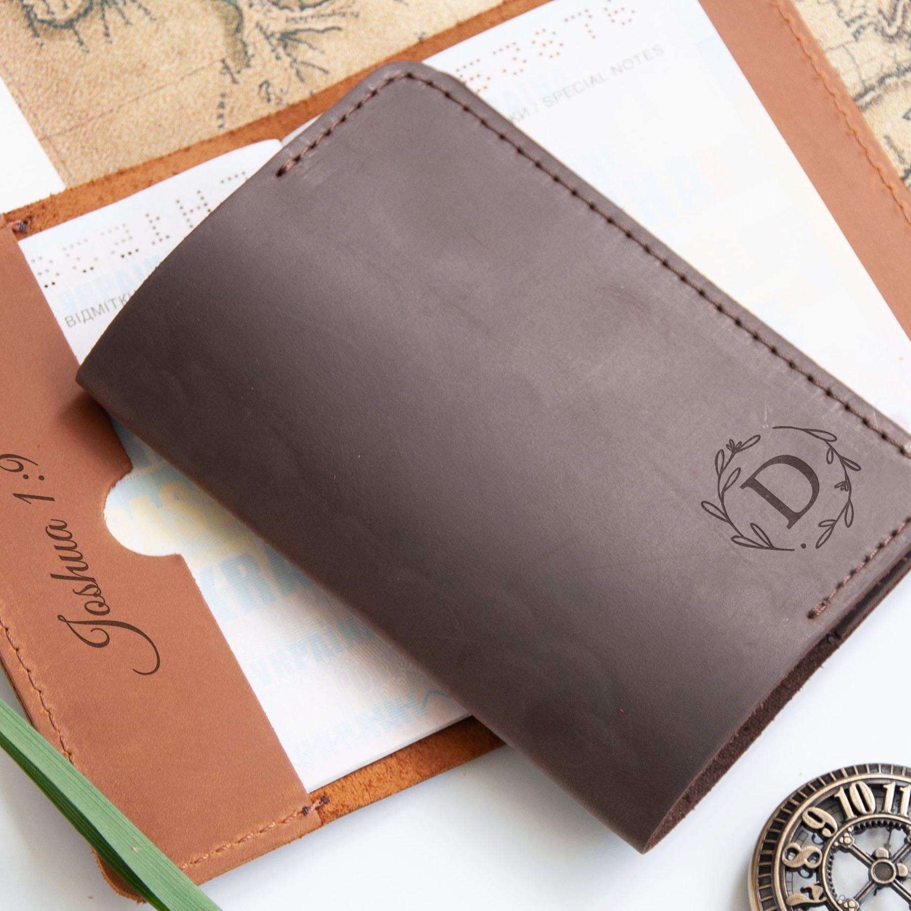 A brown leather wallet with a personalized monogrammed "D" sits on top of a piece of paper with a map and a clock.