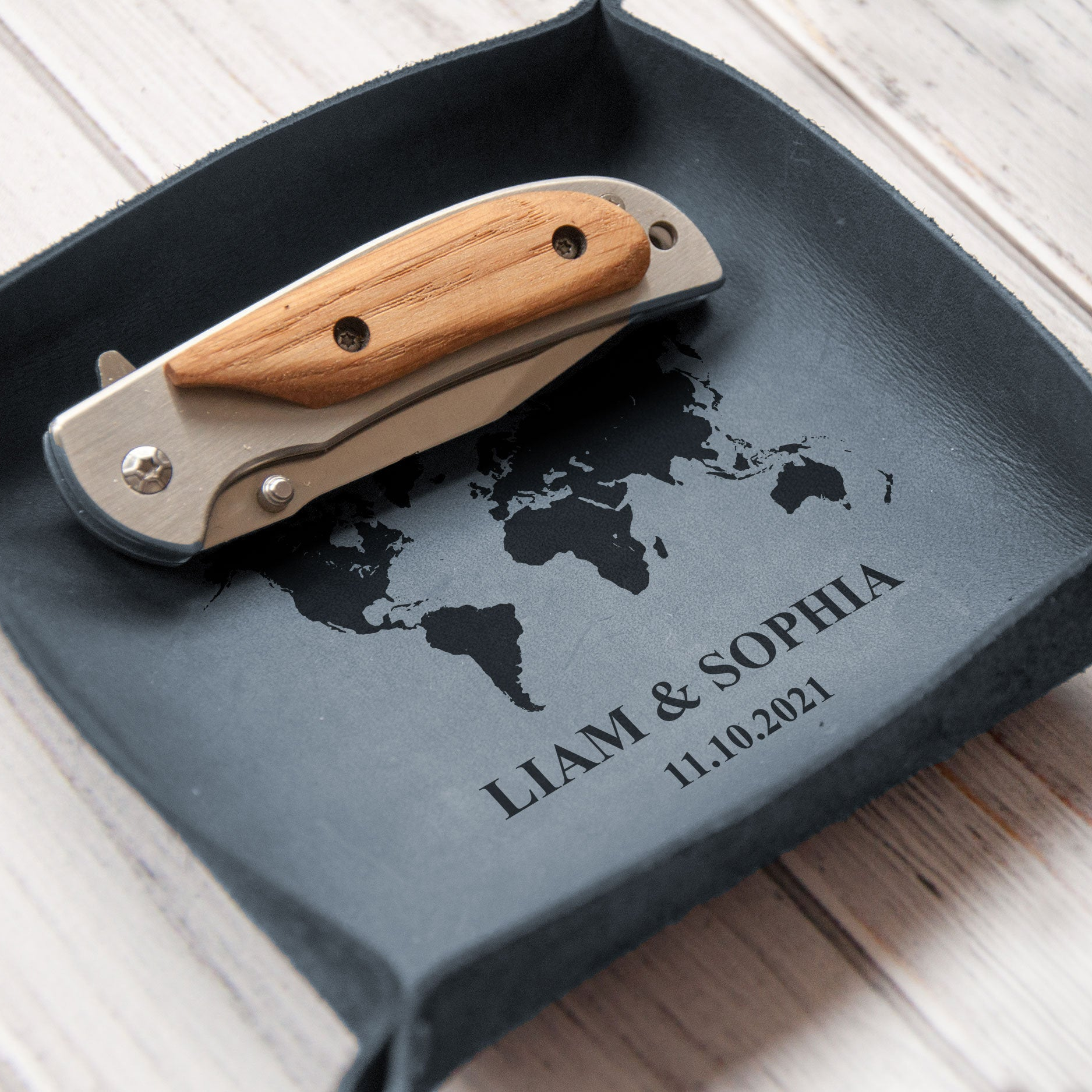 A knife with a wooden handle is placed on a gray tray with a world map design and the names "Liam & Sophia" printed on it.