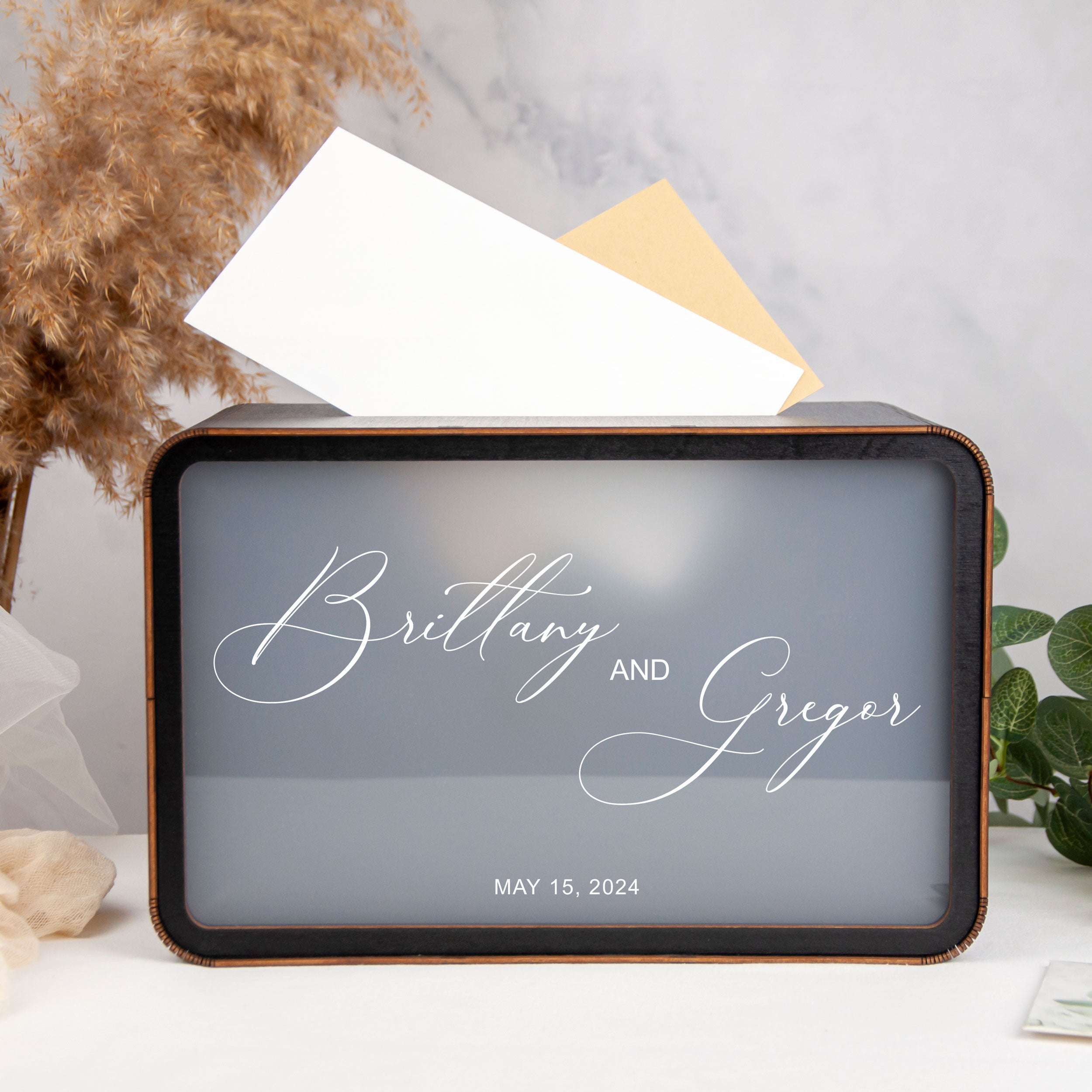 A black and white photo of a decorative box with the names 'Brittany and Gregor' written on it, along with the date 'MAY 15, 2024'.