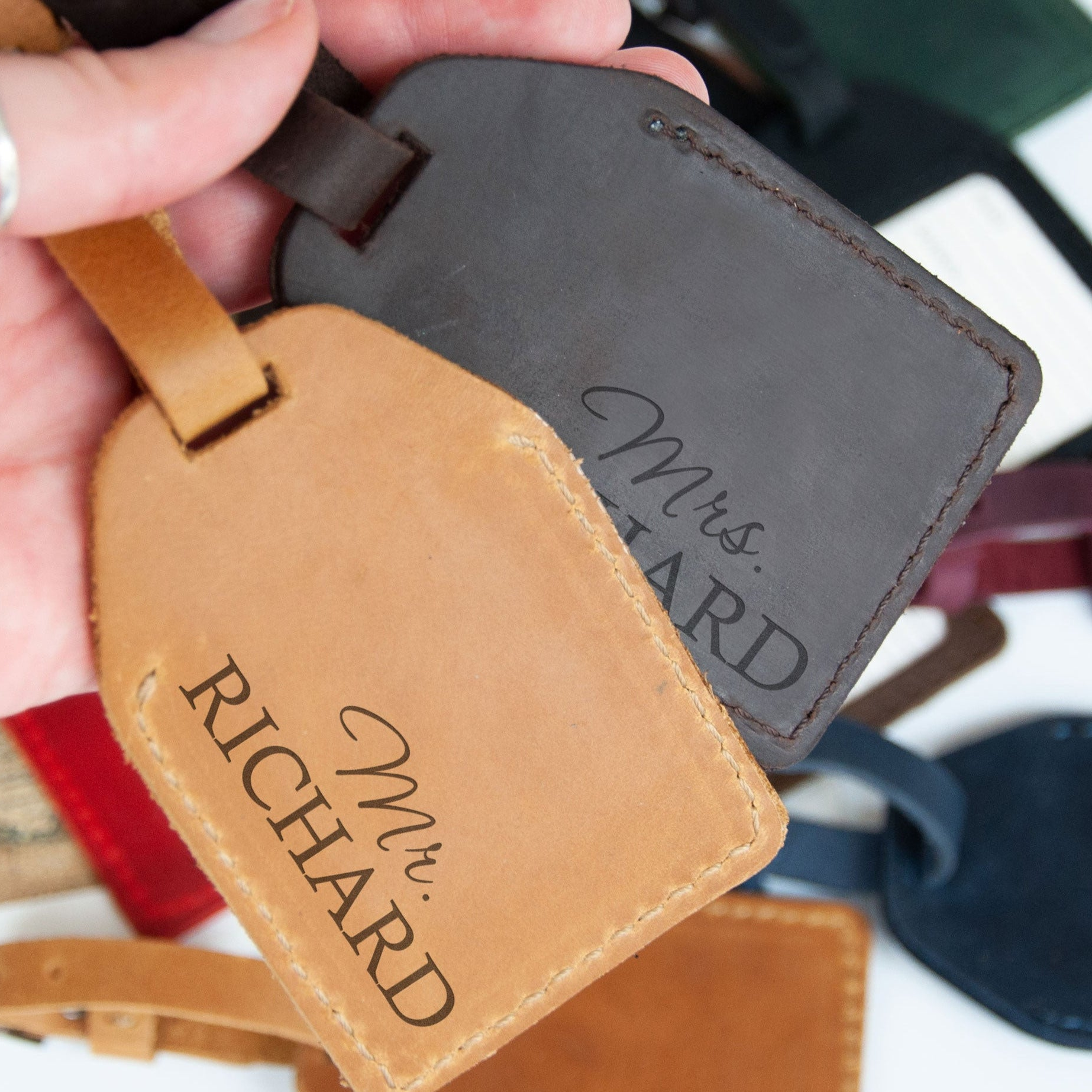A hand holding two personalized leather luggage tags with the names "Mr. Richard" printed on them.