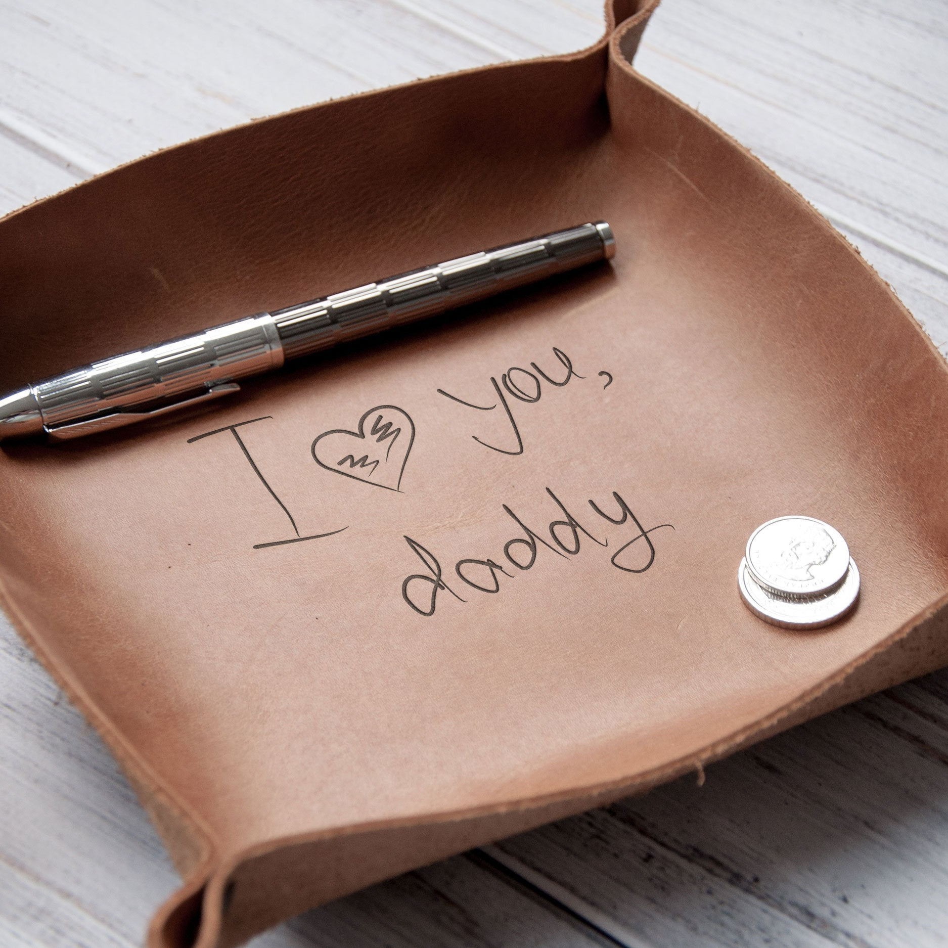 A brown leather tray with a pen and a handwritten message that says "I love you, daddy" on it.