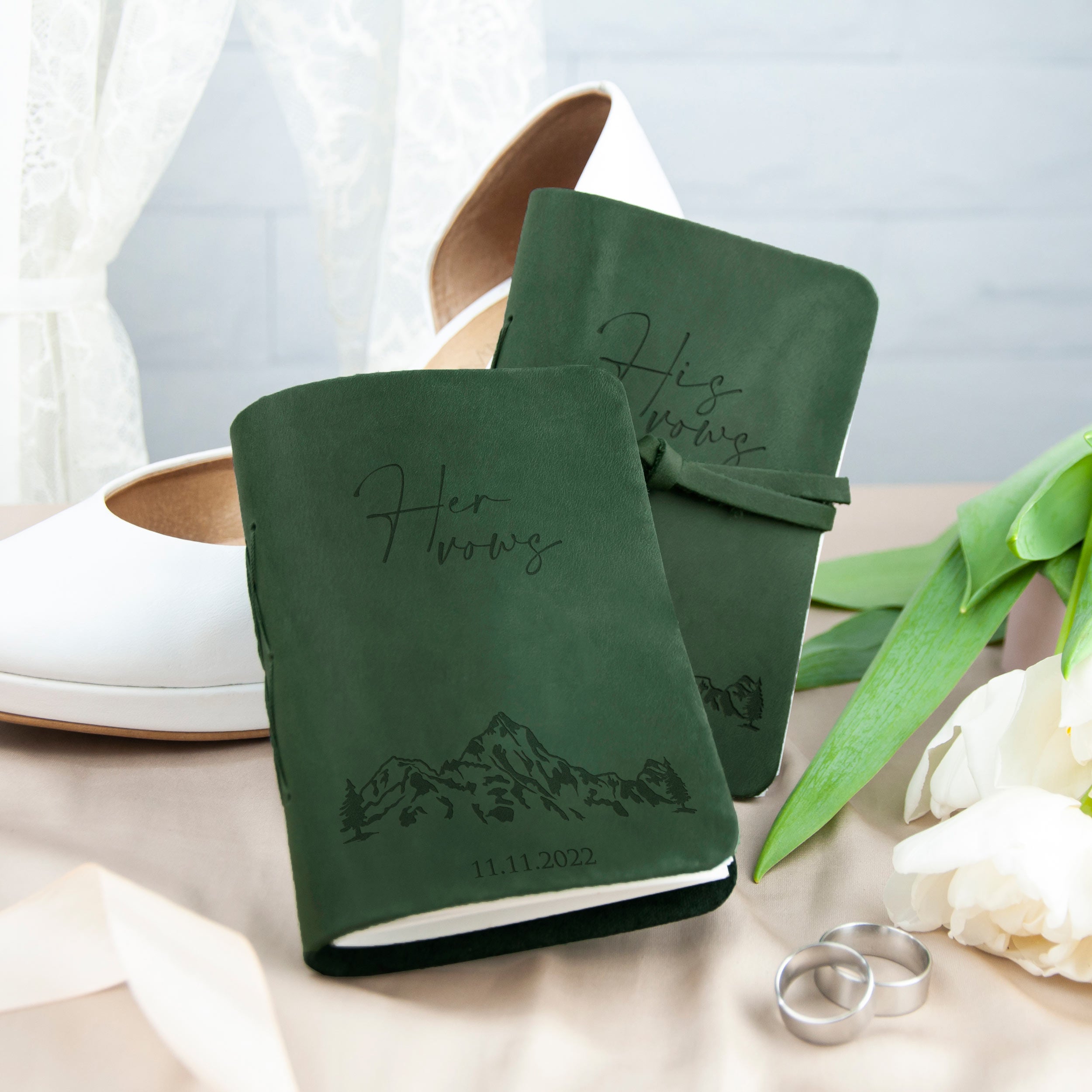 a pair of green notebooks with the text "Her Wors" printed on them, along with a pair of white shoes and a bouquet of white flowers.
