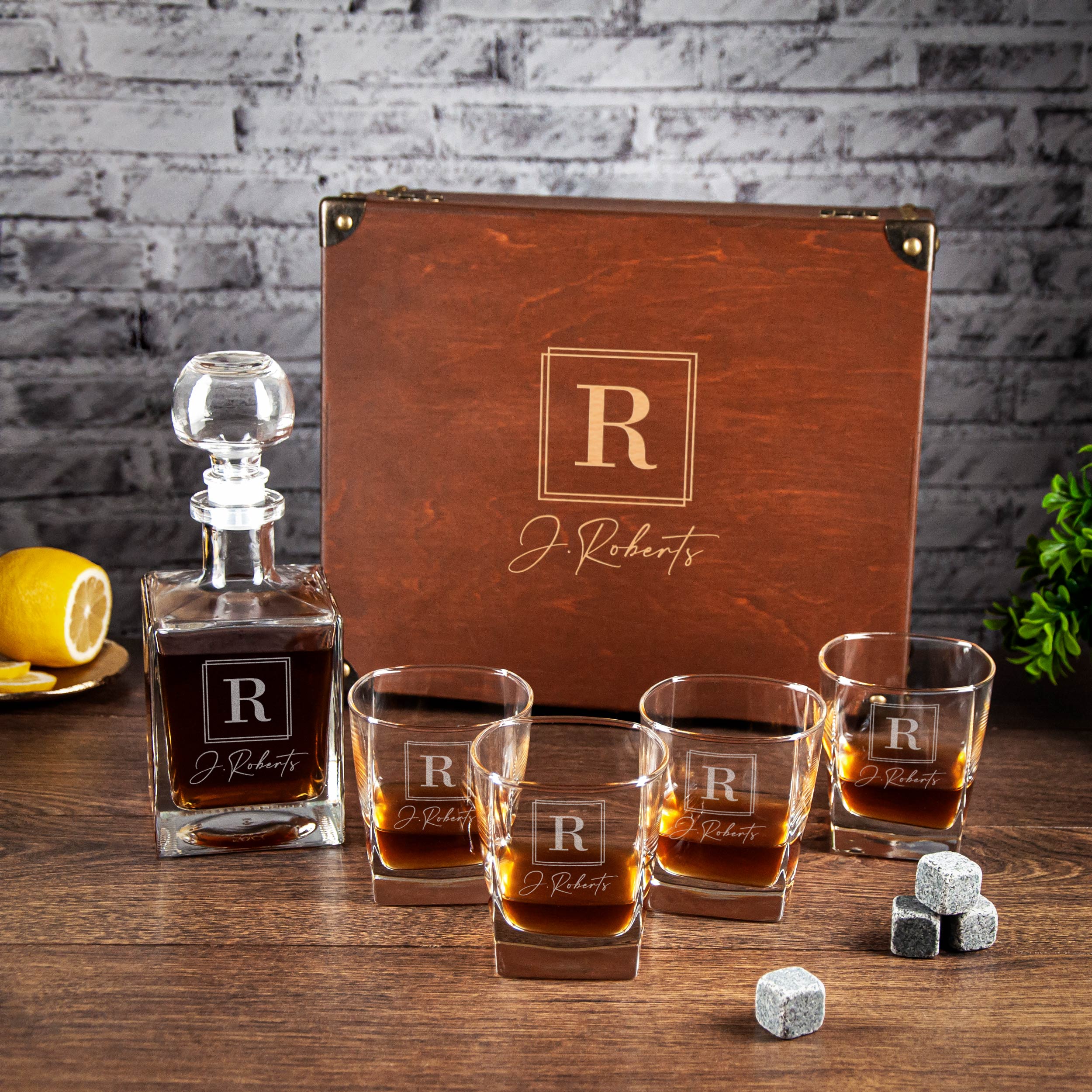 a set of whiskey glasses and a bottle of whiskey, all with personalized monogrammed labels, placed on a wooden surface.