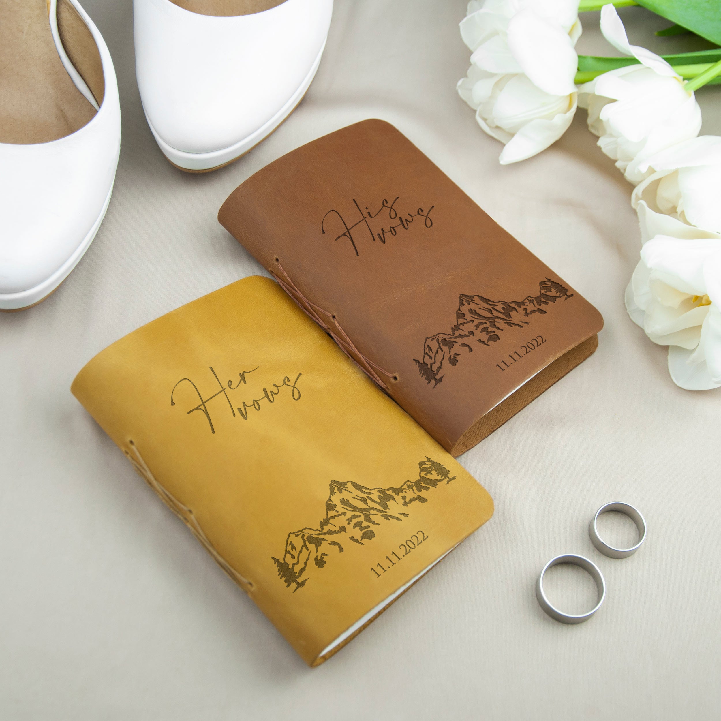 a pair of leather-bound notebooks with the names "Her Wishes" and "His Wishes" printed on them, along with a pair of silver wedding rings and a pair of white shoes.