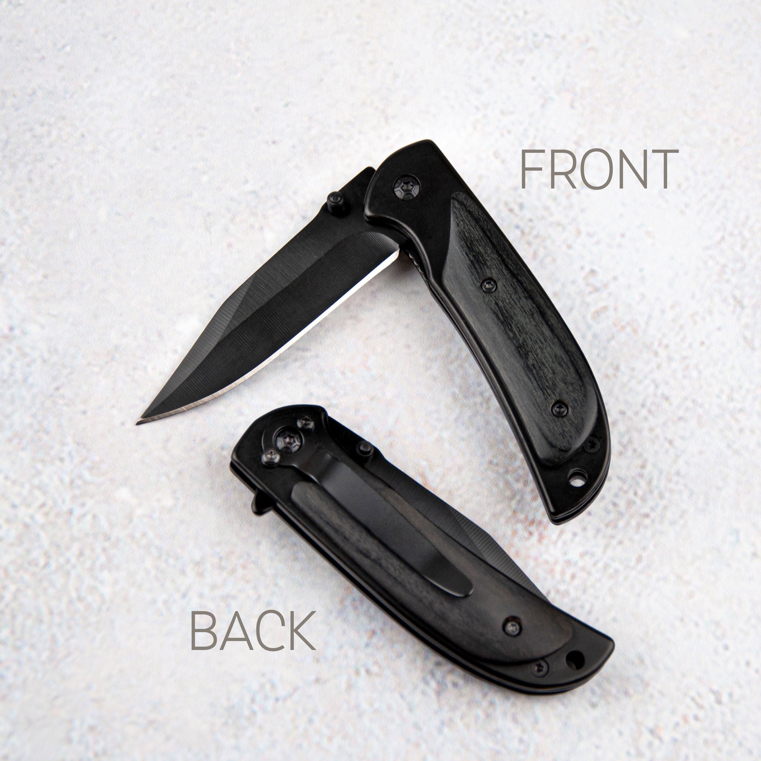 two black pocket knives, one with the blade facing up and the other with the blade facing down, both resting on a white surface.