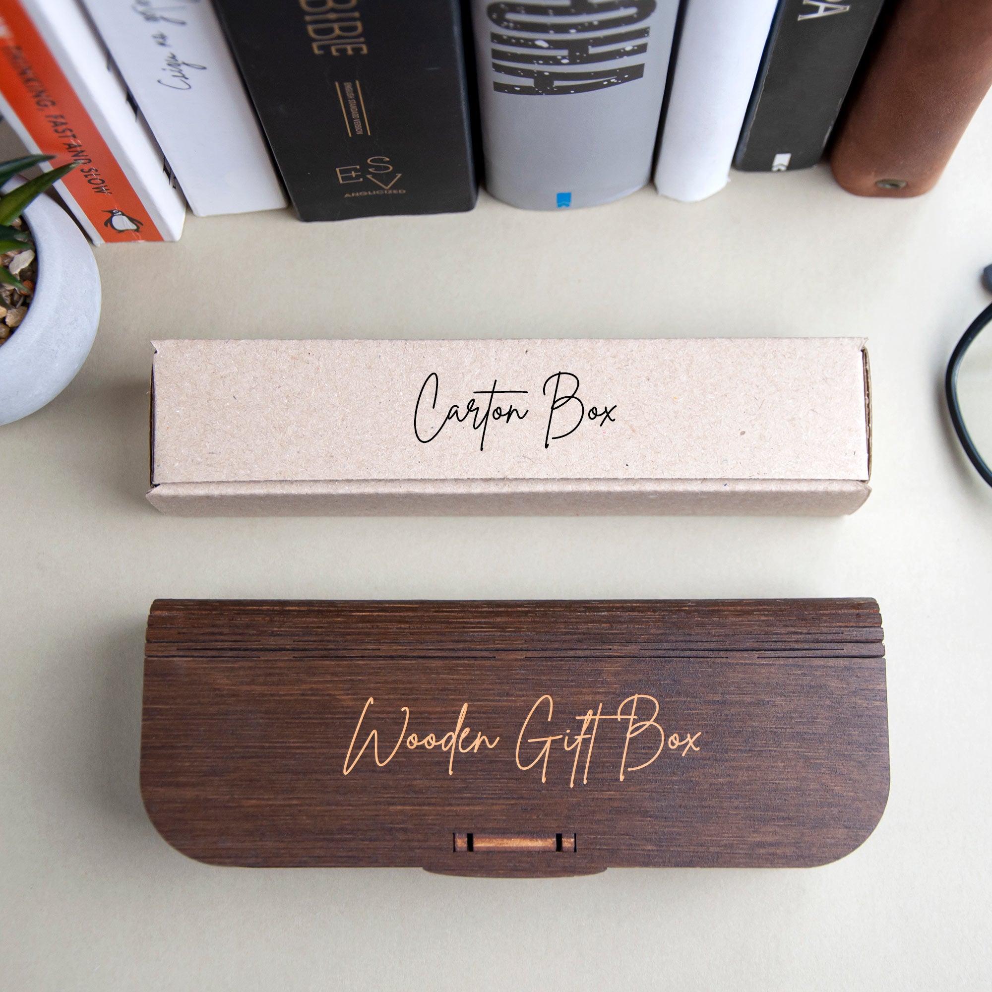 two wooden gift boxes, one brown and one beige, placed on a table next to a stack of books.