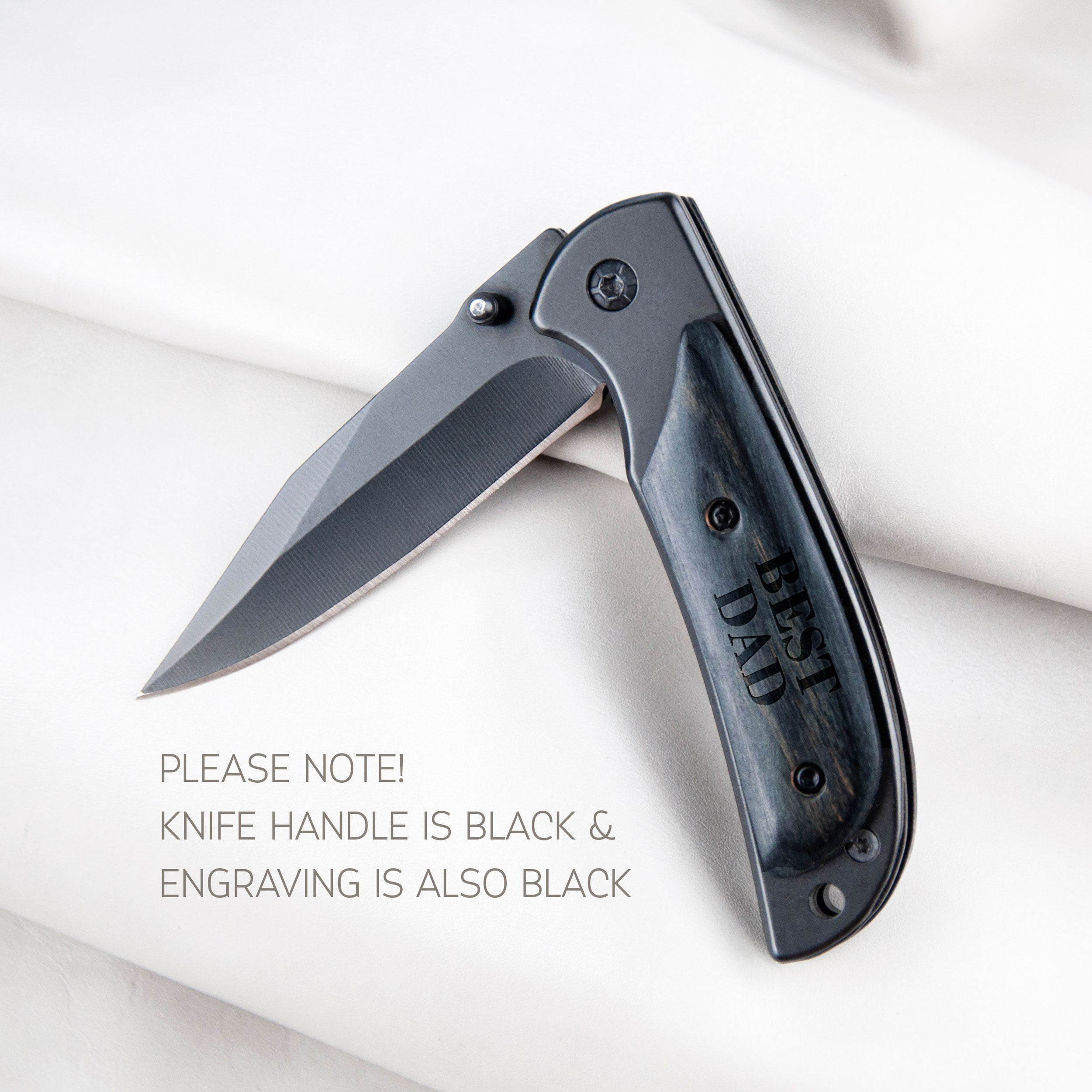 A black knife with a handle engraved with the text "BEST DAD" is shown on a white surface.