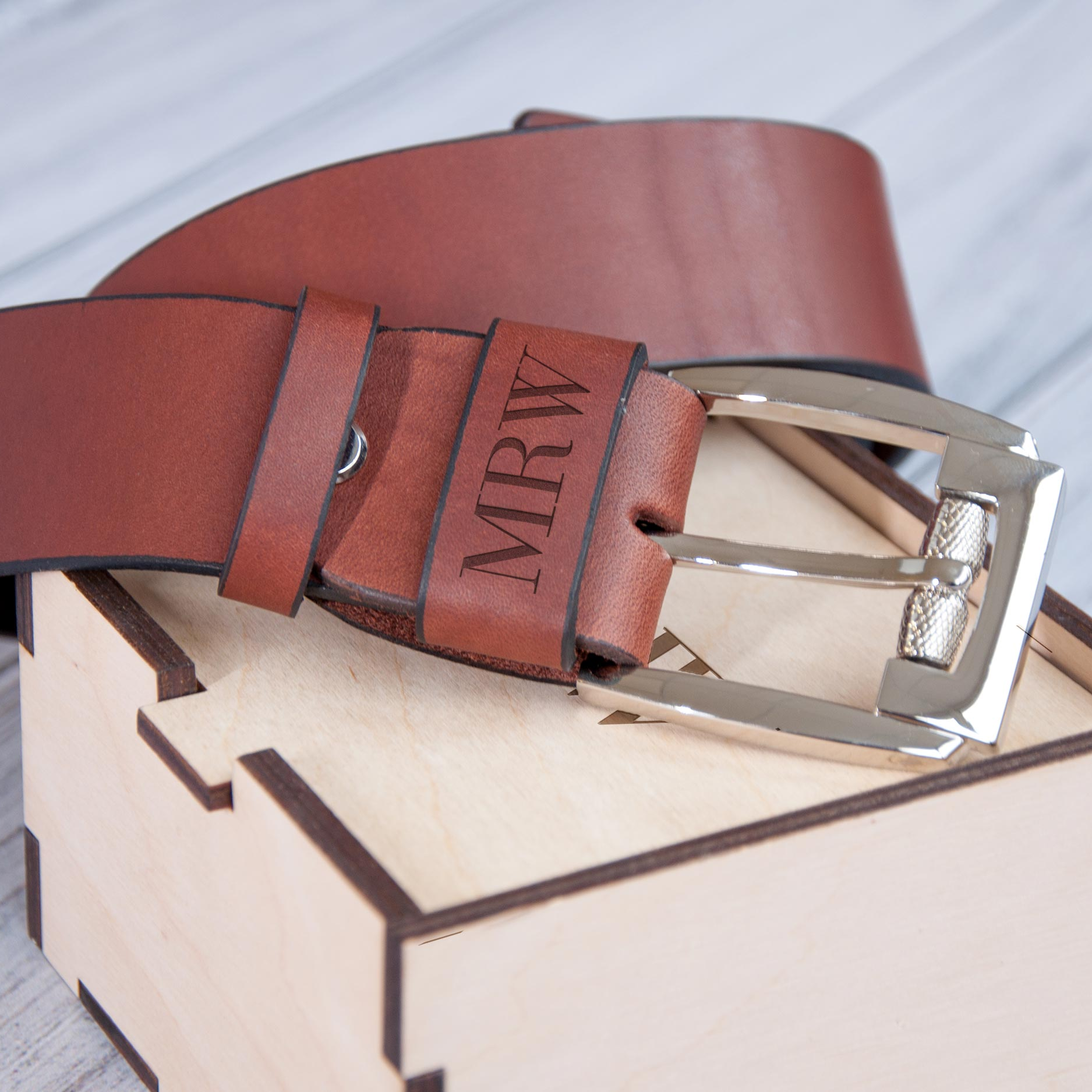 A brown leather belt with a silver buckle is placed on top of a wooden box.