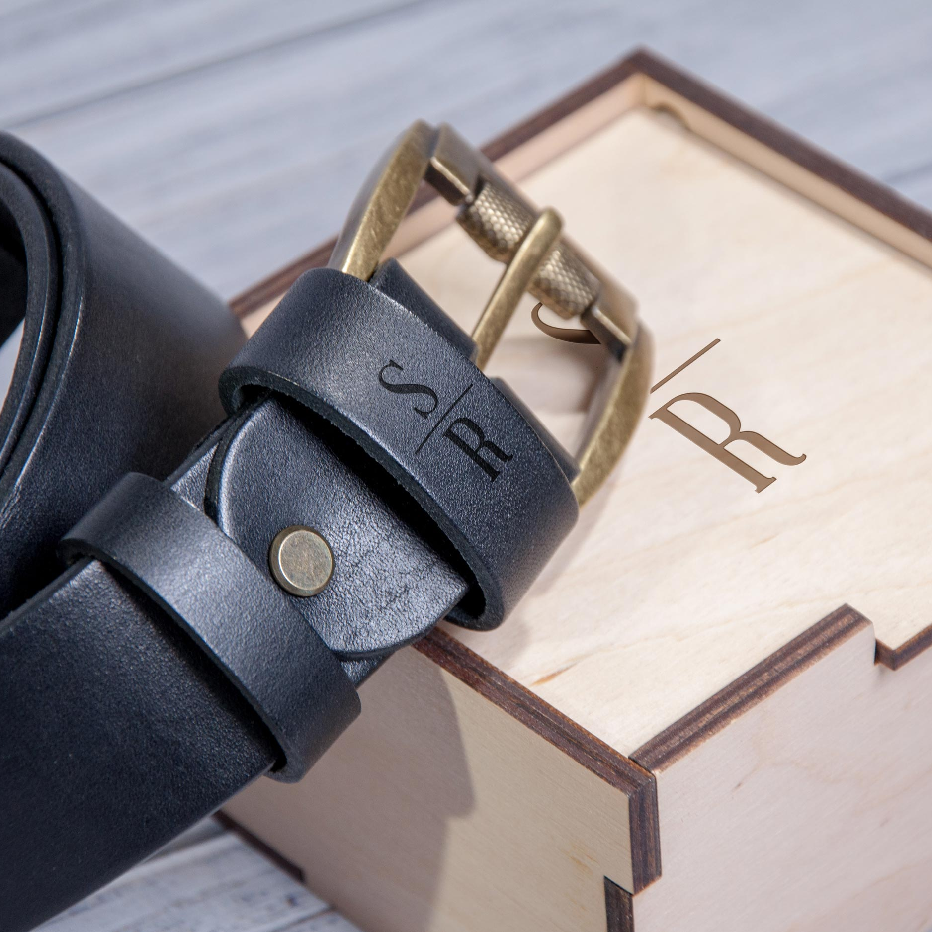 A black leather belt with a gold buckle is placed on top of a wooden box with a lid.