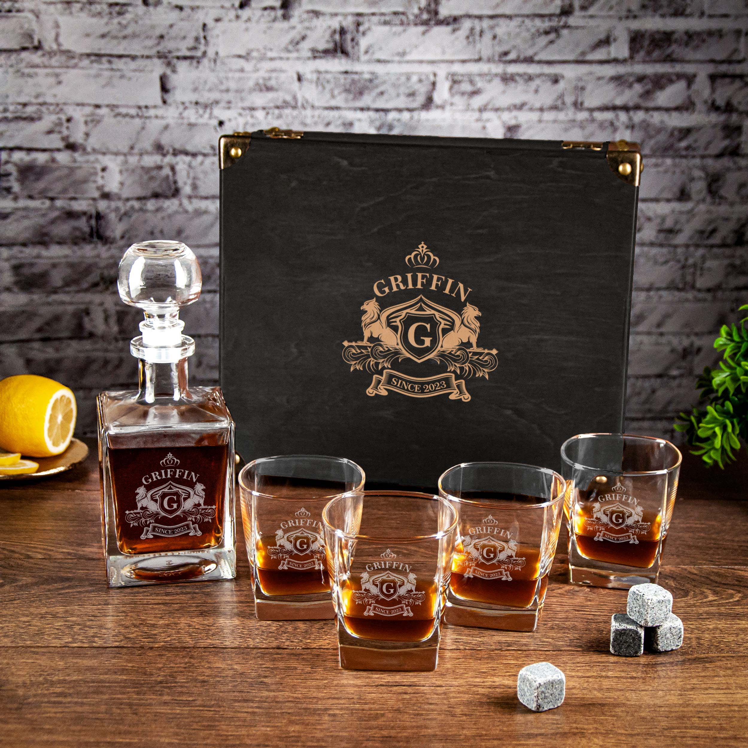 A set of four glasses filled with amber-colored whiskey, accompanied by a bottle of whiskey and a black case with the word "GRIFFIN" printed on it, all placed on a wooden surface against a brick wall background.