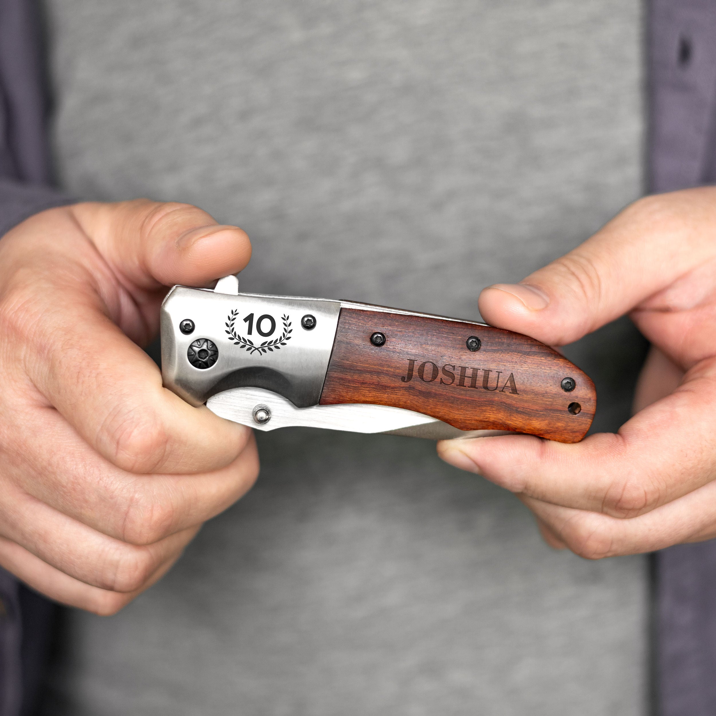 A person's hands holding a knife with the name "Joshua" engraved on it.
