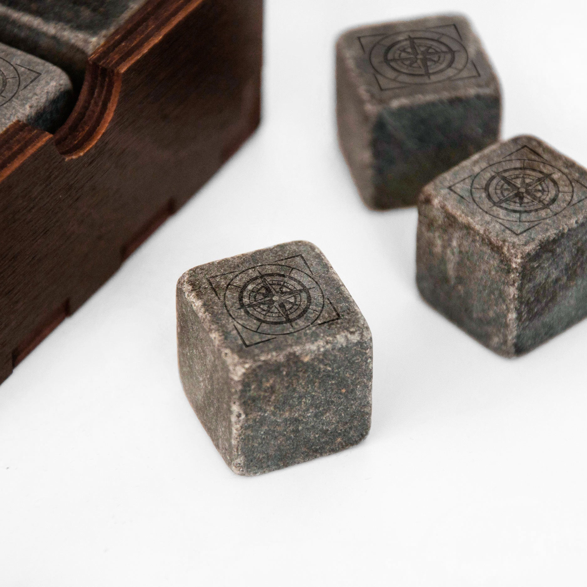 three square-shaped stones with a compass design on them, placed on a white surface next to a wooden box.