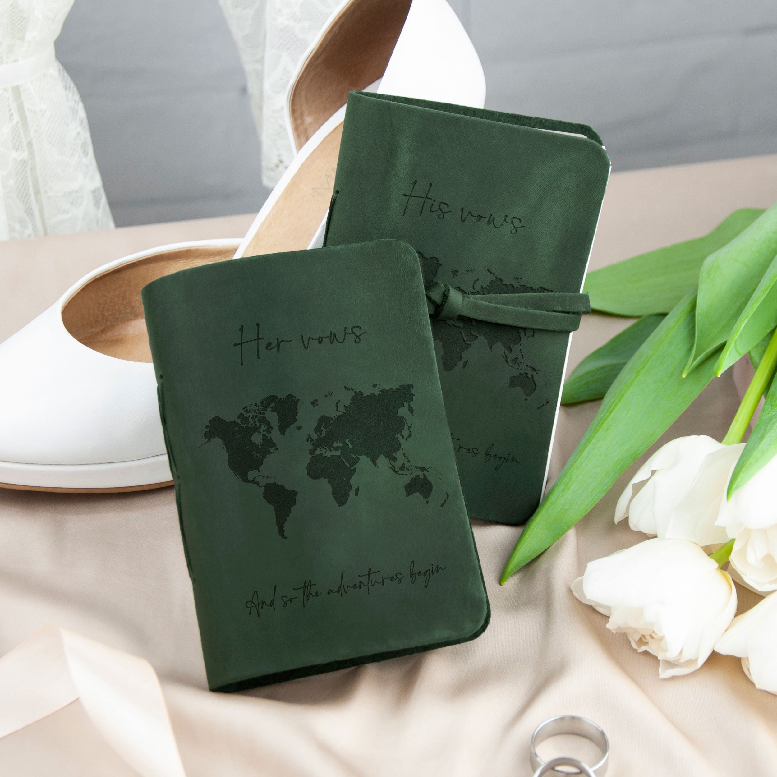 a pair of green notebooks with a world map design, placed on a table alongside a pair of white shoes and some white flowers.